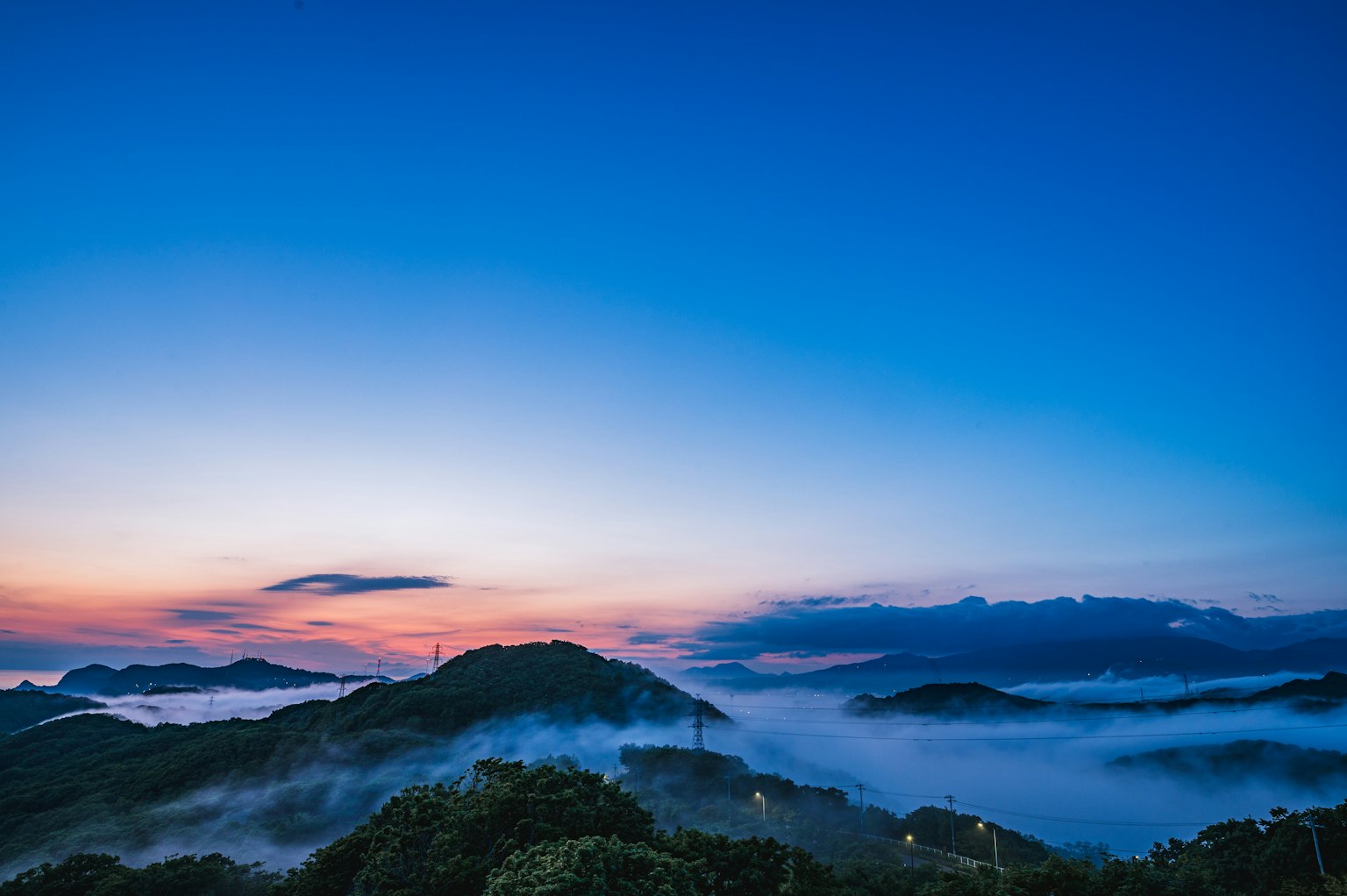 Vista panoramica di colline avvolte nella nebbia sotto un cielo blu