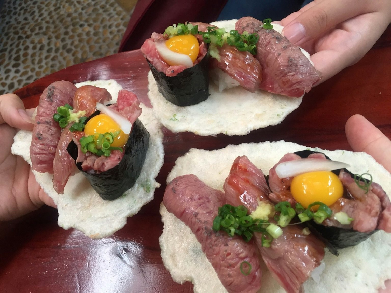 Sushi dengan kuning telur dan daun bawang di atas kerupuk beras yang dipegang di tangan