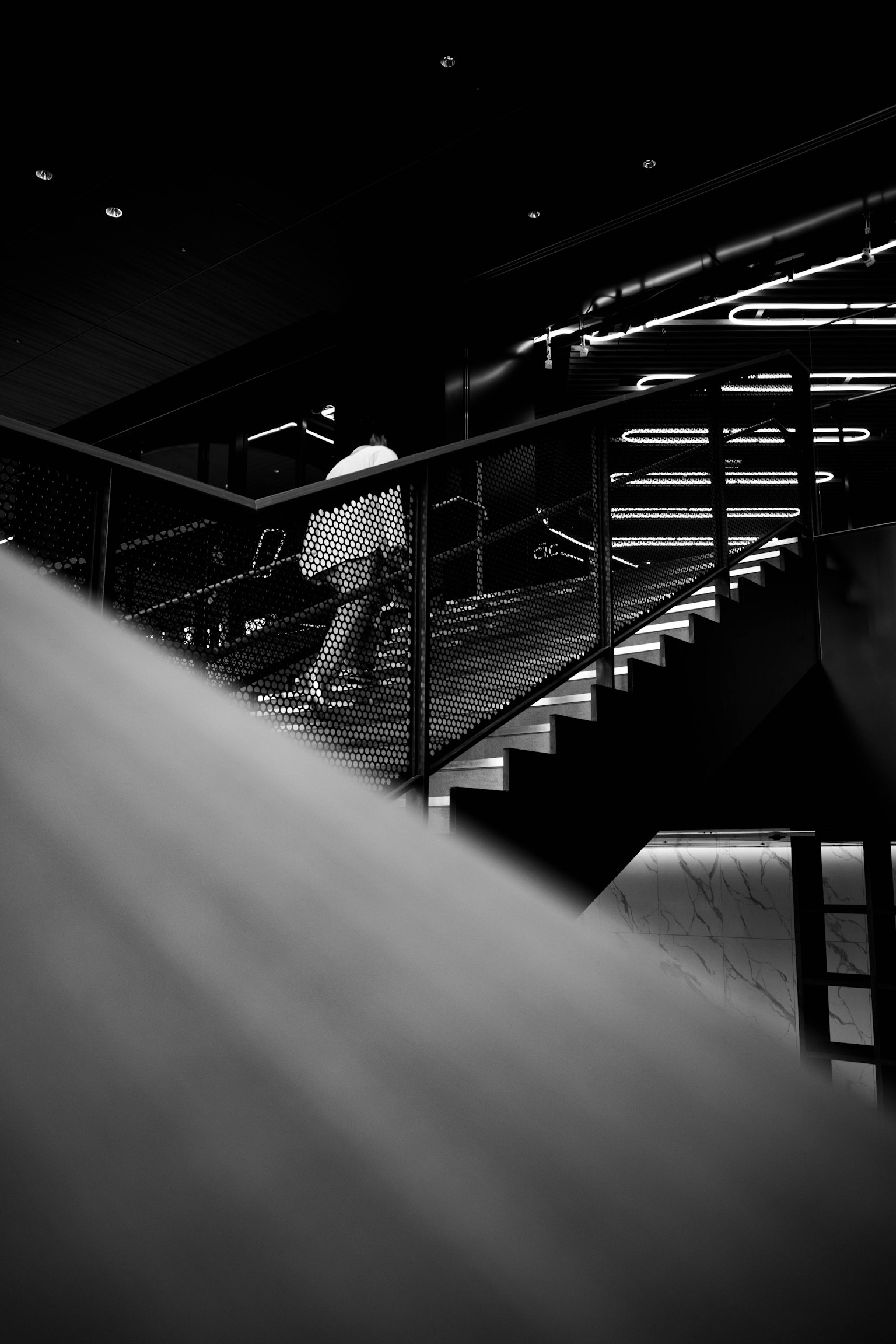 Schwarzweißbild einer Person, die eine Treppe hinaufsteigt, mit starkem Kontrast von Licht und Schatten