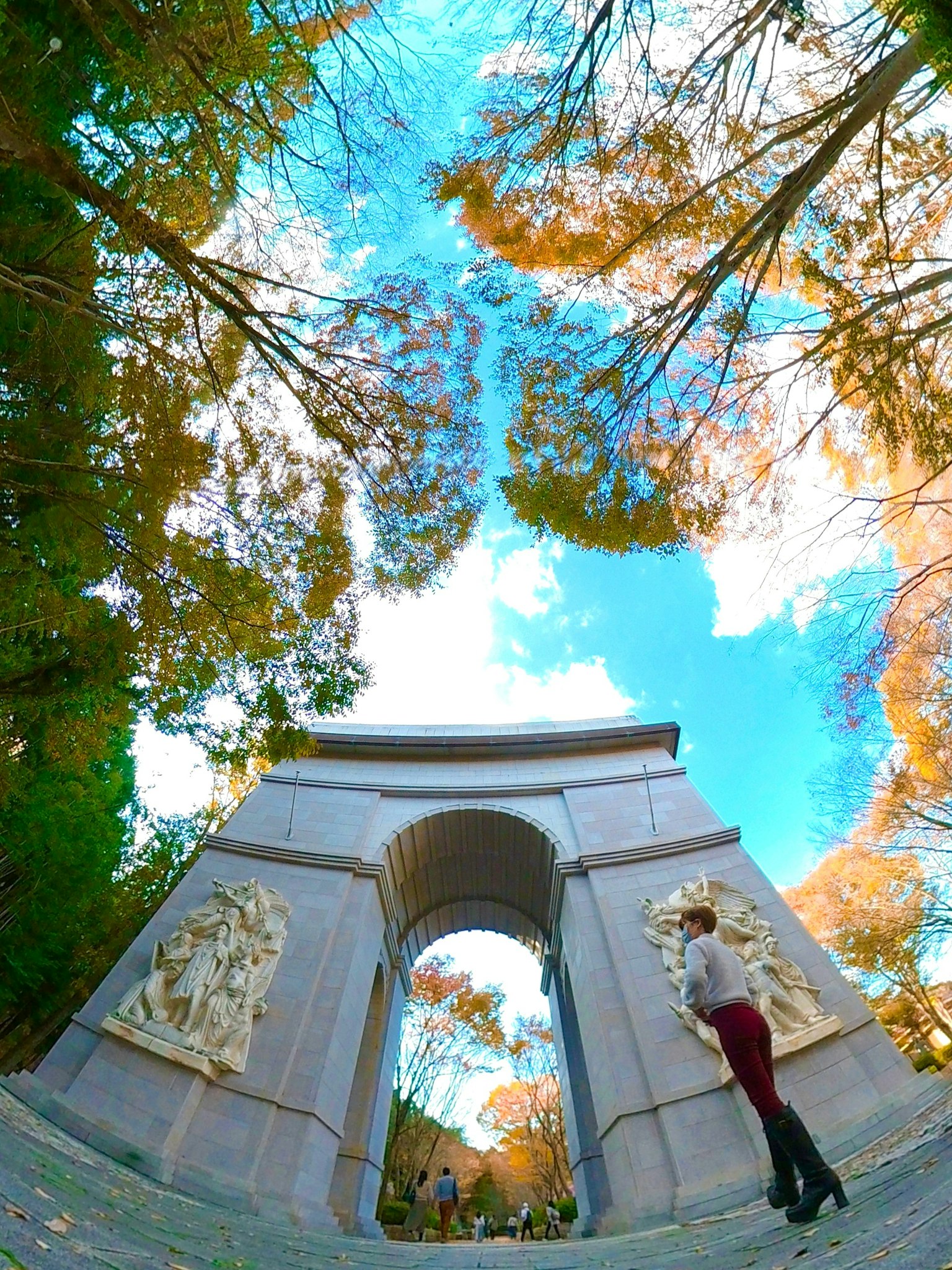 Una donna in piedi sotto un arco circondata da alberi colorati e un cielo blu