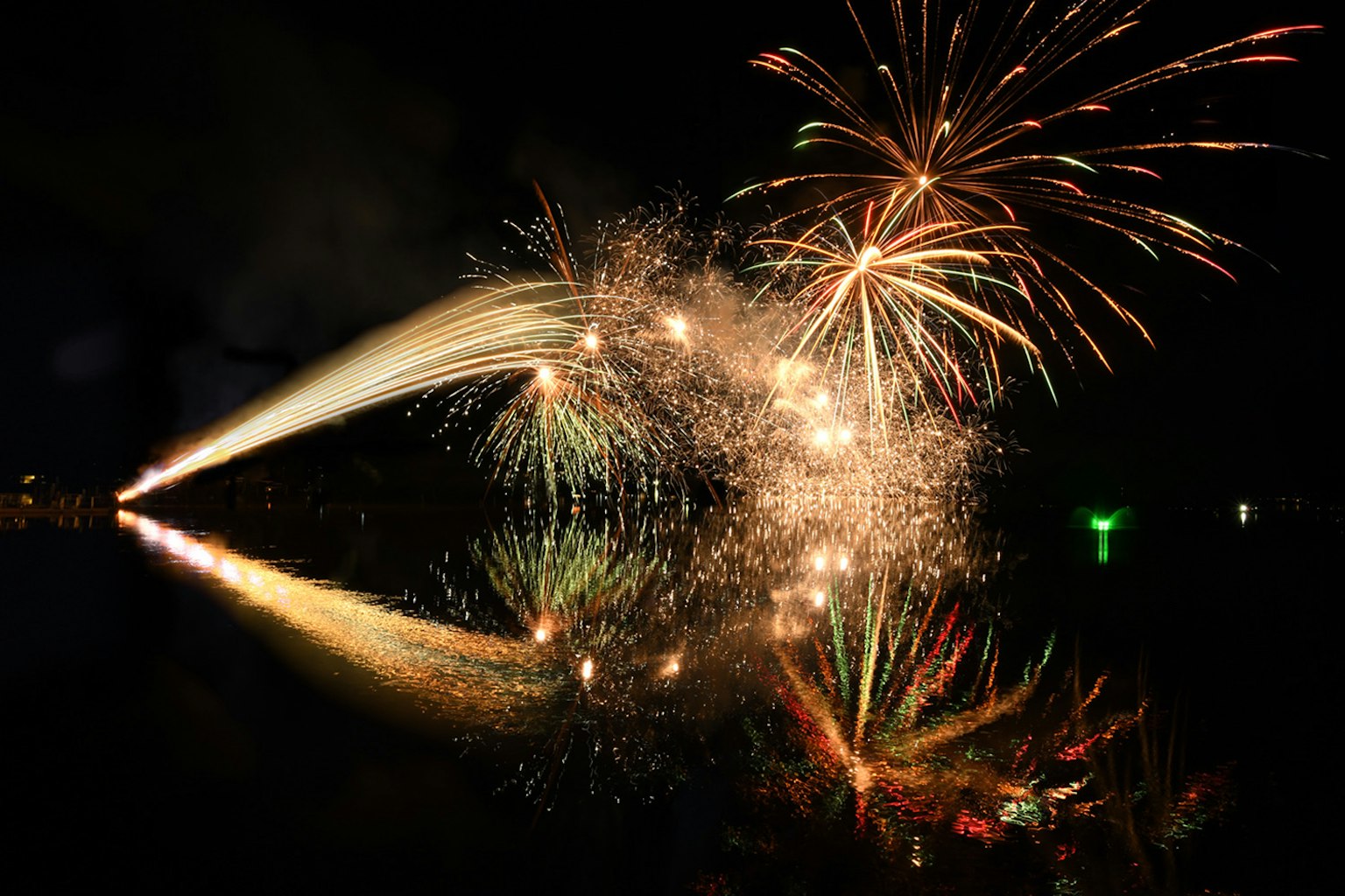 Schöne Feuerwerk-Show am Nachthimmel mit bunten Reflexionen auf der Wasseroberfläche