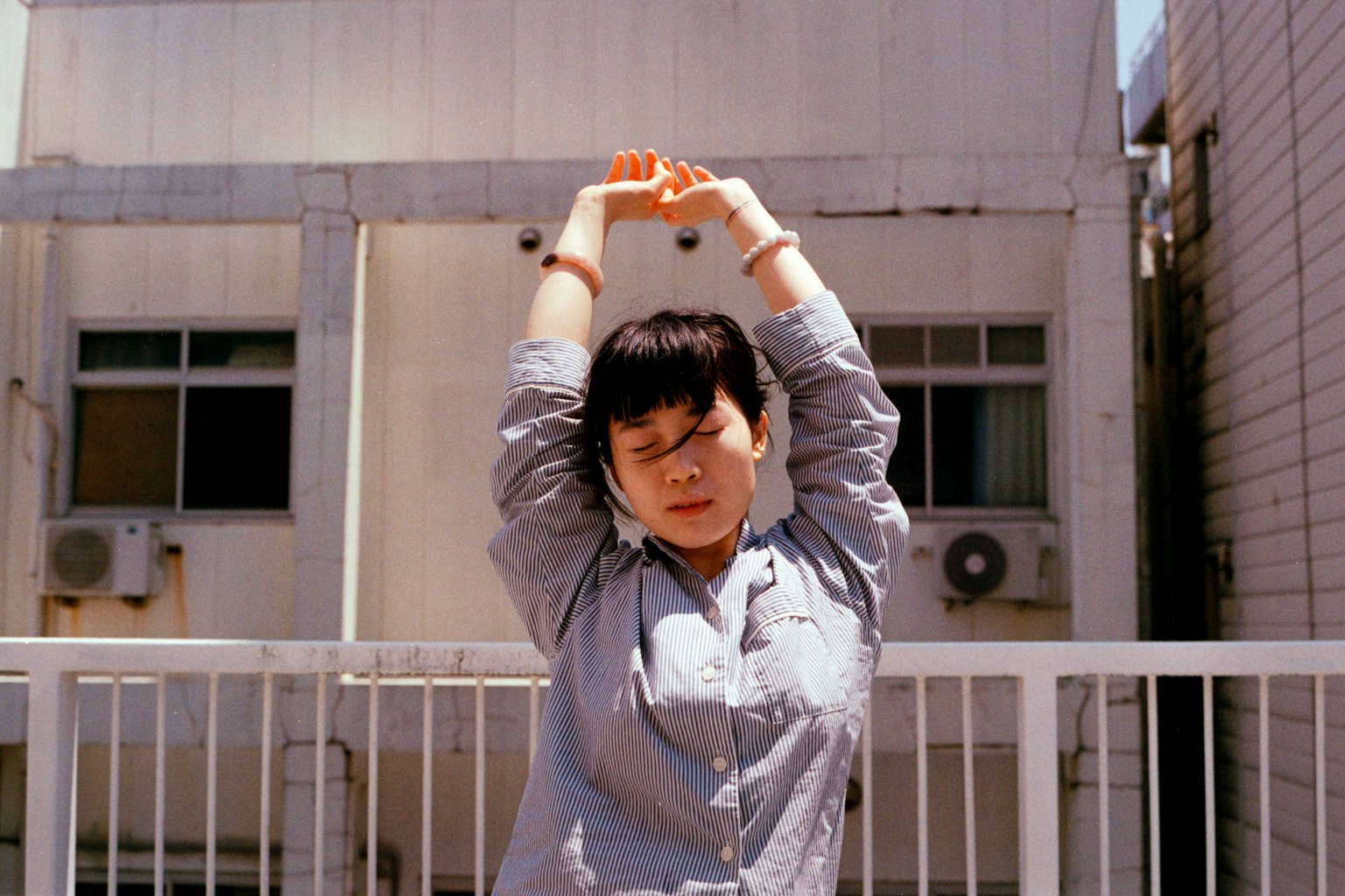 A woman stretching outdoors with buildings and air conditioning units in the background
