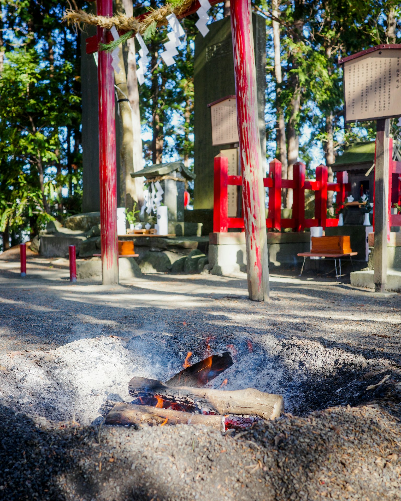 一幅风景画，展示了一个有红色柱子的神社和一个被灰烬包围的火堆