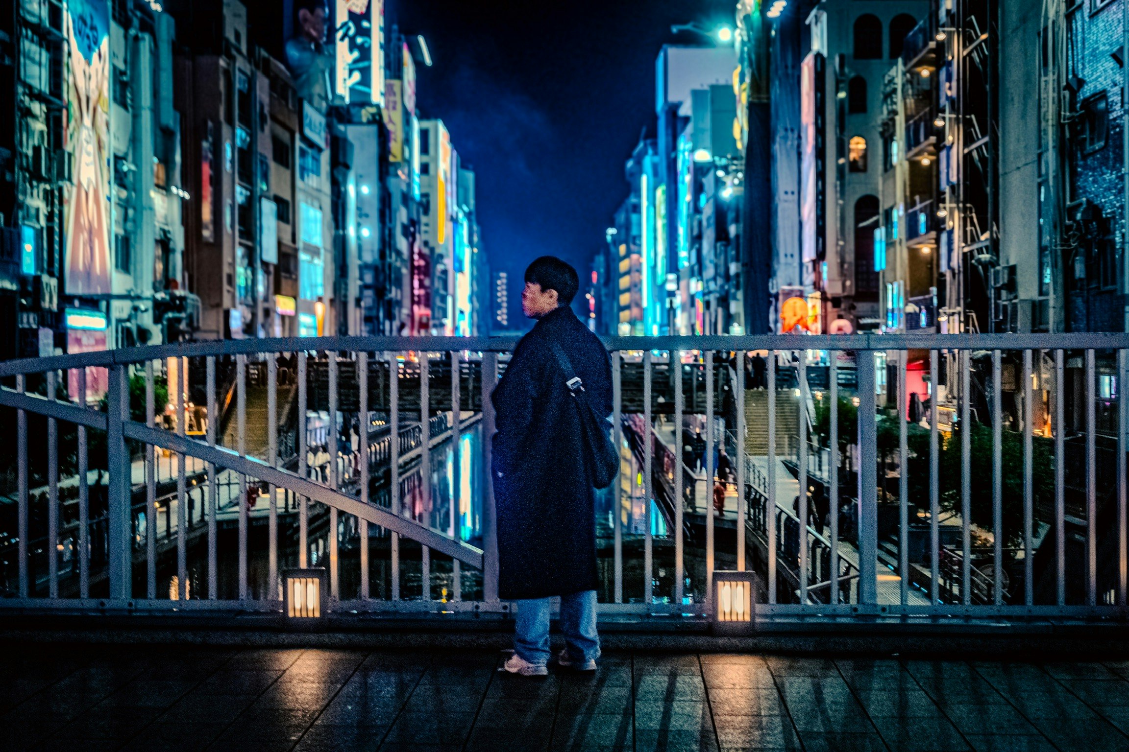 難波の夜のネオンが並ぶ路地の橋上で佇む人物