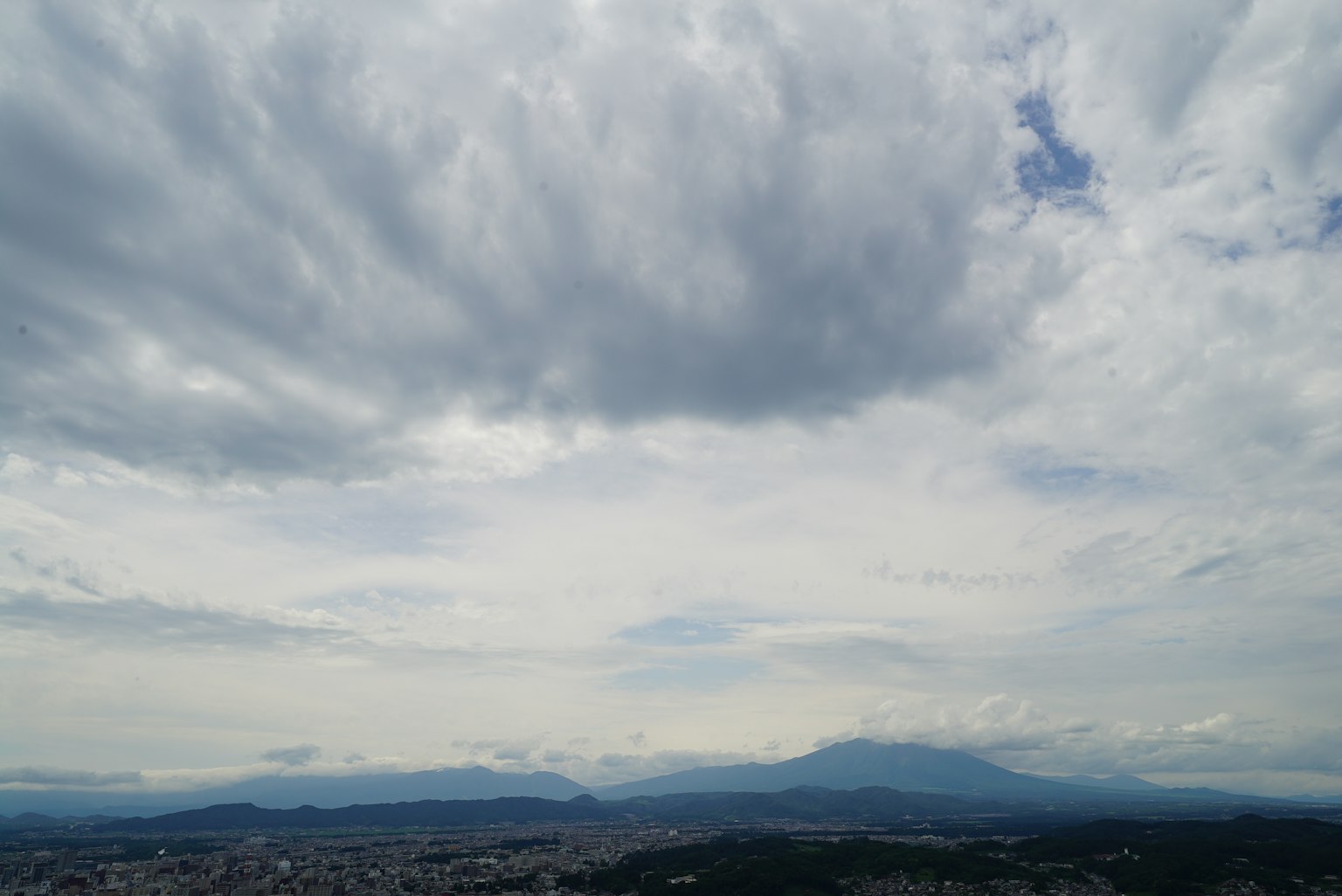 Langit berawan dengan pegunungan jauh dan pemandangan kota