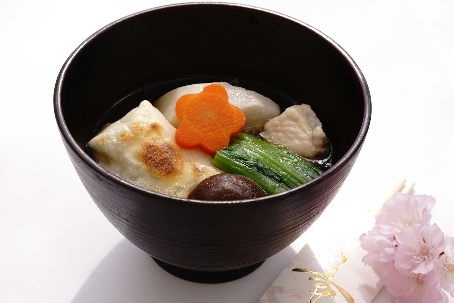 Zuppa giapponese in una ciotola nera con pollo verdure e una carota a forma di fiore