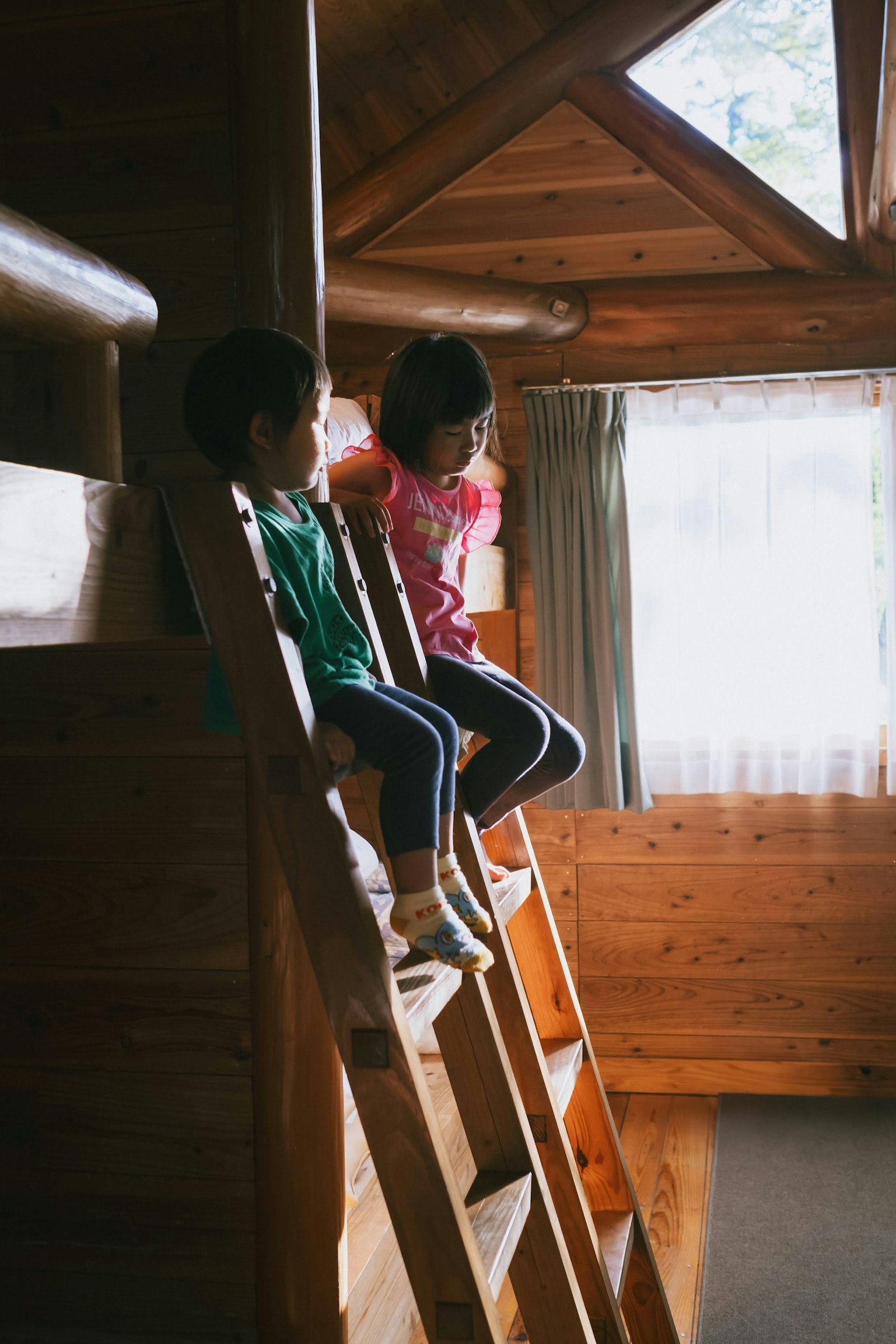 木製のはしごに座る二人の子供たち 明るい窓からの自然光が差し込む温かみのある木の内装