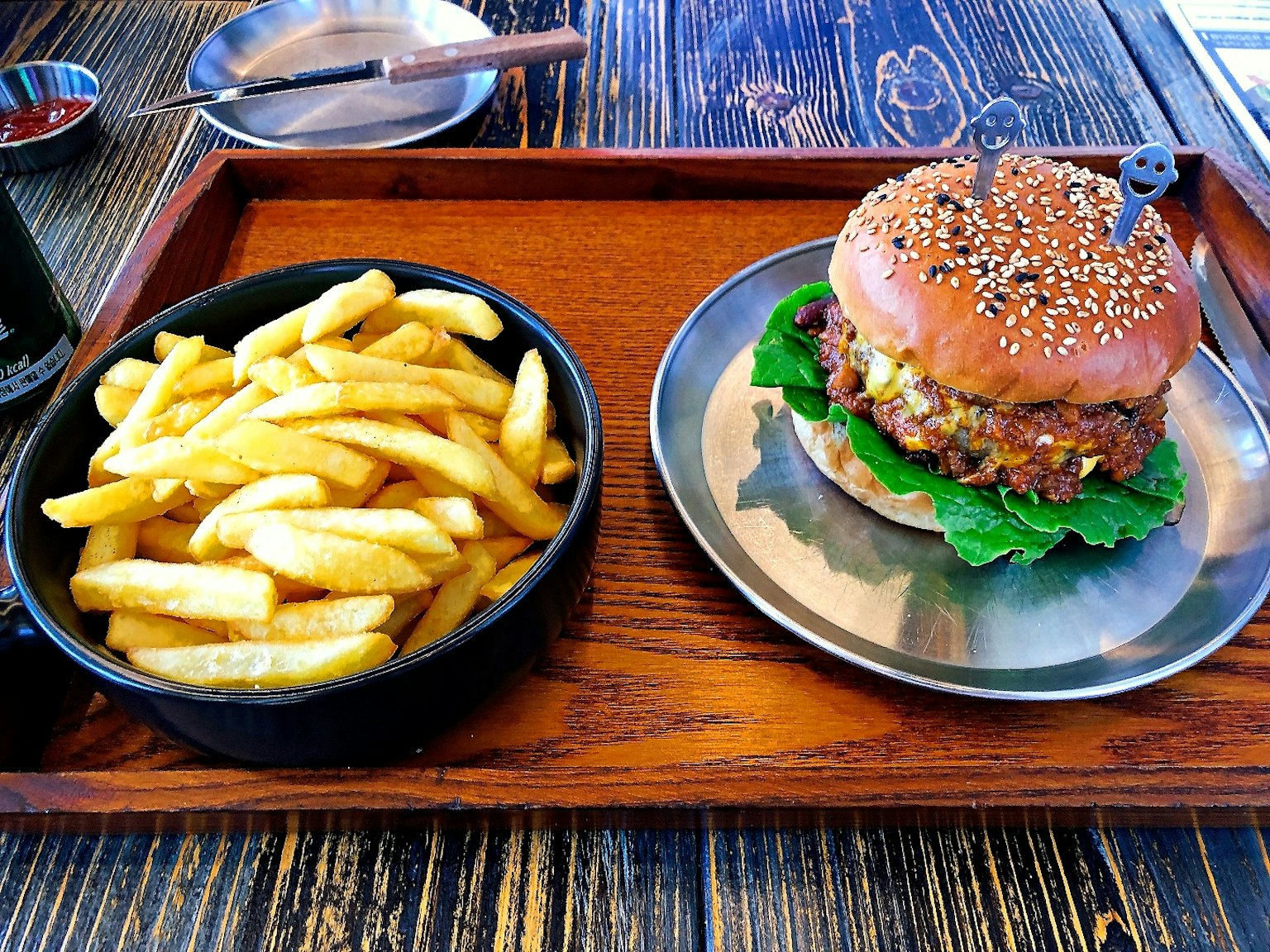 A sesame seed bun burger with lettuce and fries on a wooden tray