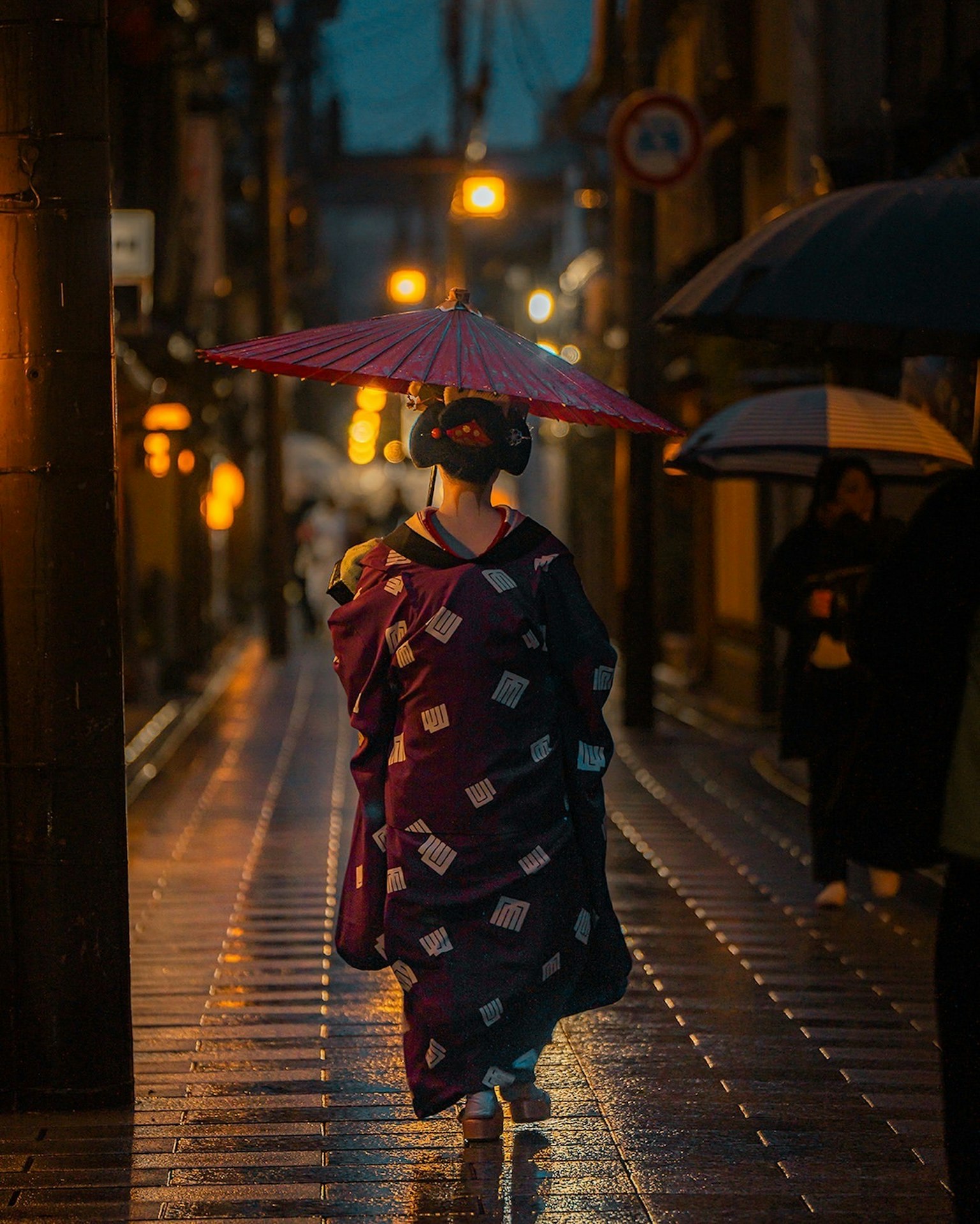 Femme en kimono marchant dans la rue la nuit avec un parapluie