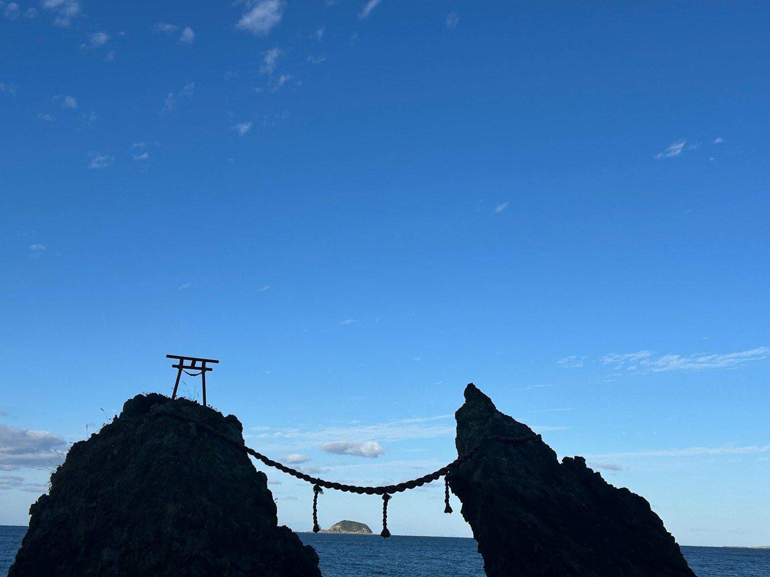 Deux rochers avec un pont et un torii entre eux sous un ciel bleu