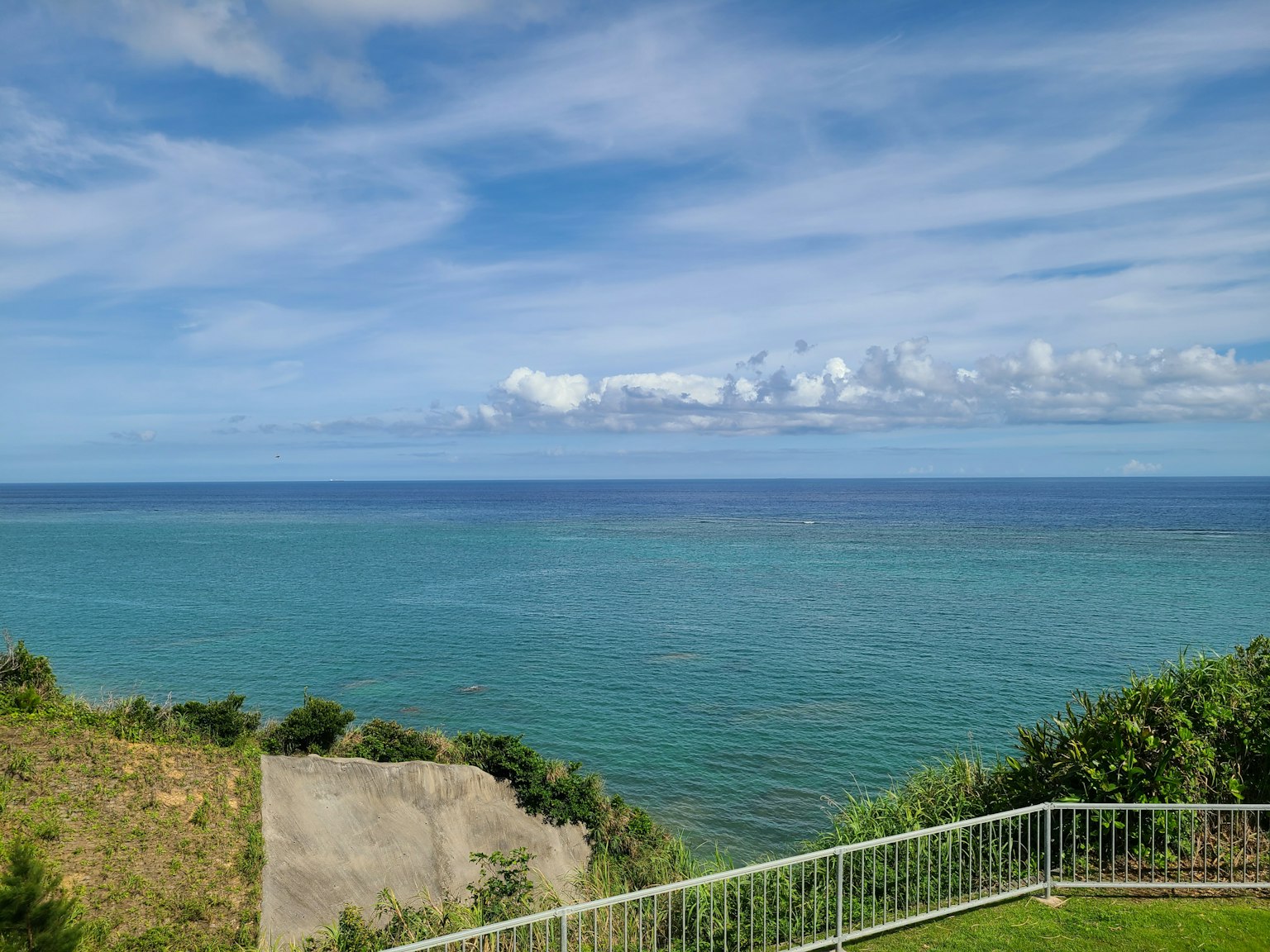 Malersicher Blick auf den blauen Ozean und den Himmel mit grünen Hügeln und einem weißen Zaun