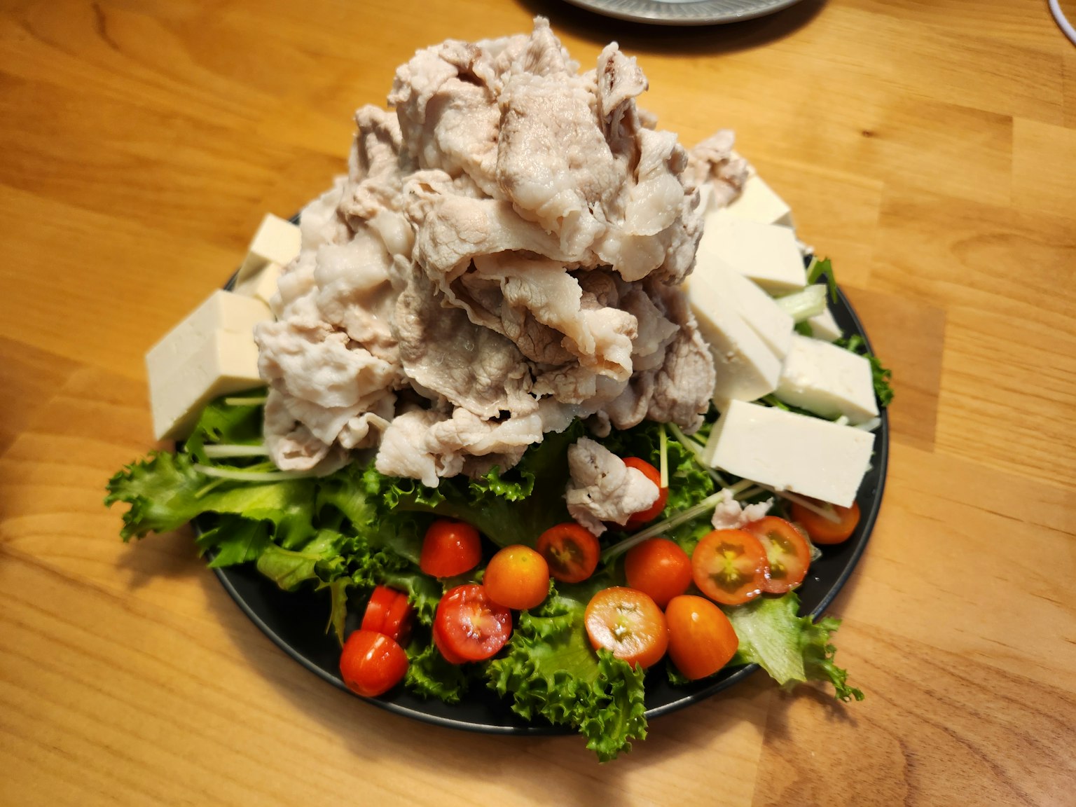 Un plato con pollo desmenuzado y tofu sobre una cama de verduras y tomates cherry
