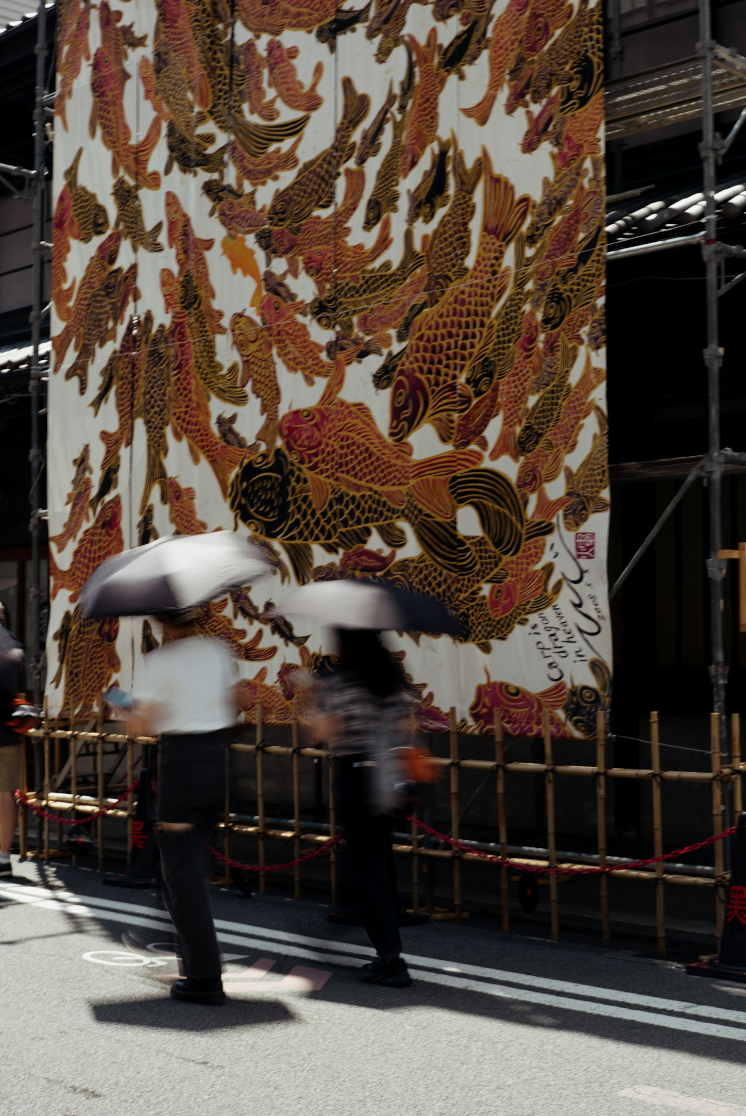 People walking with umbrellas in front of a large fabric featuring fish patterns