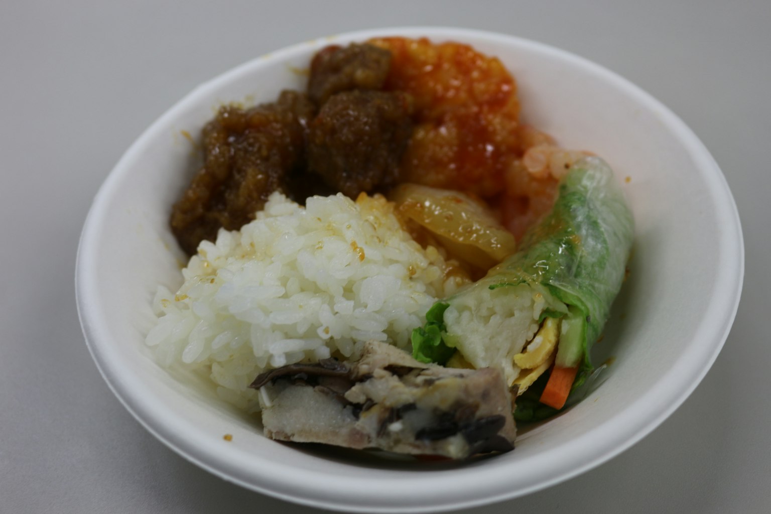 一个碗里有米饭、肉丸、橙色酱汁和蔬菜春卷