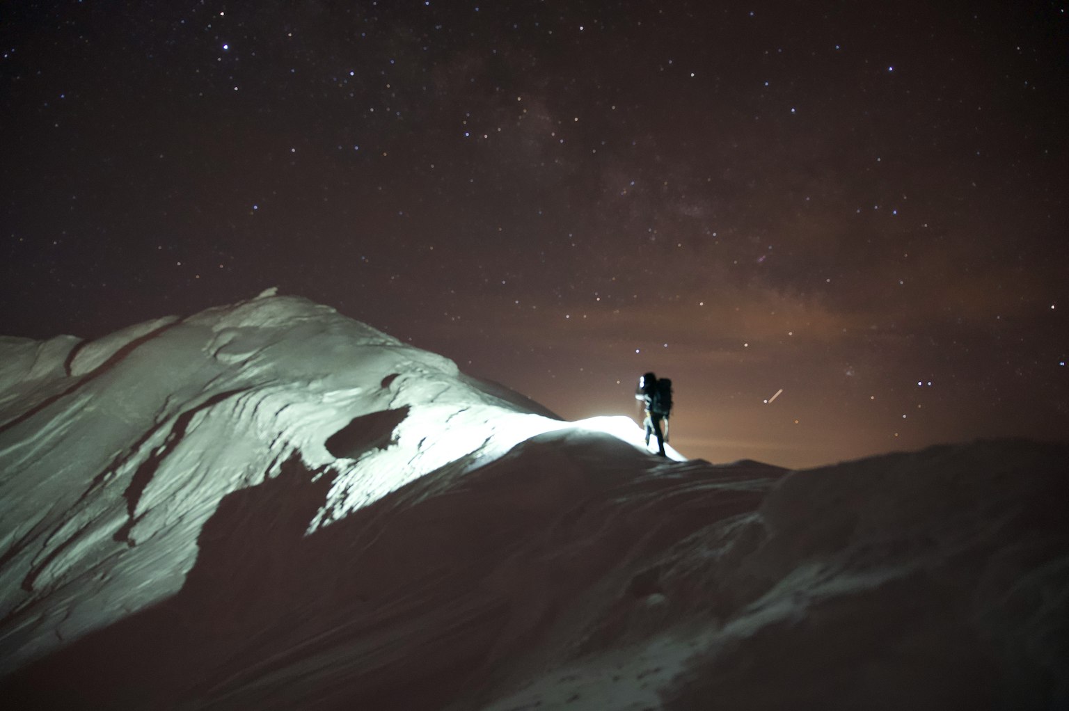 Silhouette eines Kletterers auf einem verschneiten Berg unter einem sternenklaren Nachthimmel
