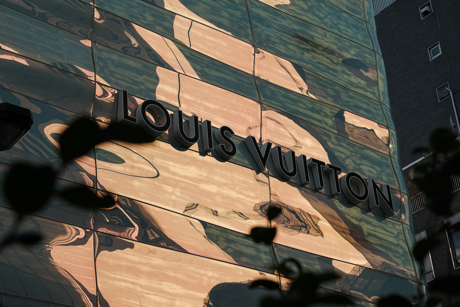 Facciata del negozio Louis Vuitton con superficie riflettente e silhouette di piante