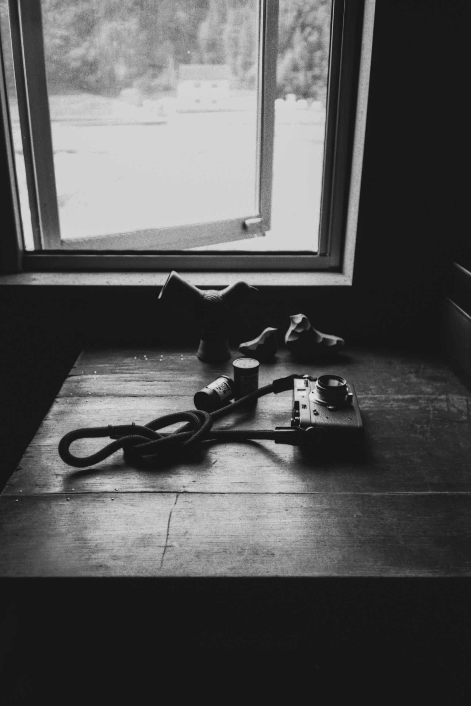 Foto in bianco e nero di una macchina fotografica e scarpe su un tavolo vicino a una finestra