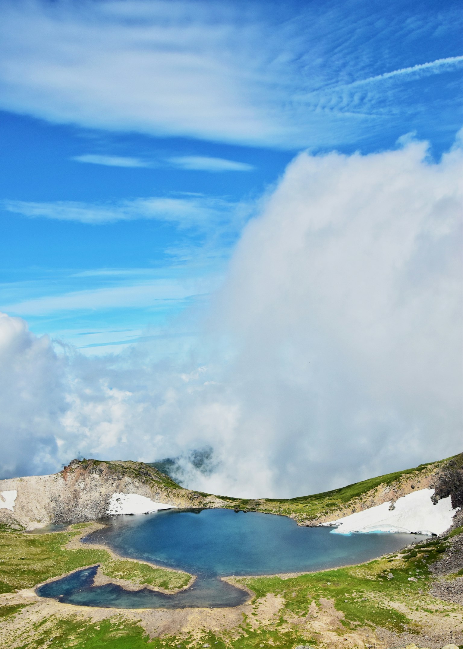 Beautiful lake at the mountain summit surrounded by blue sky and white clouds