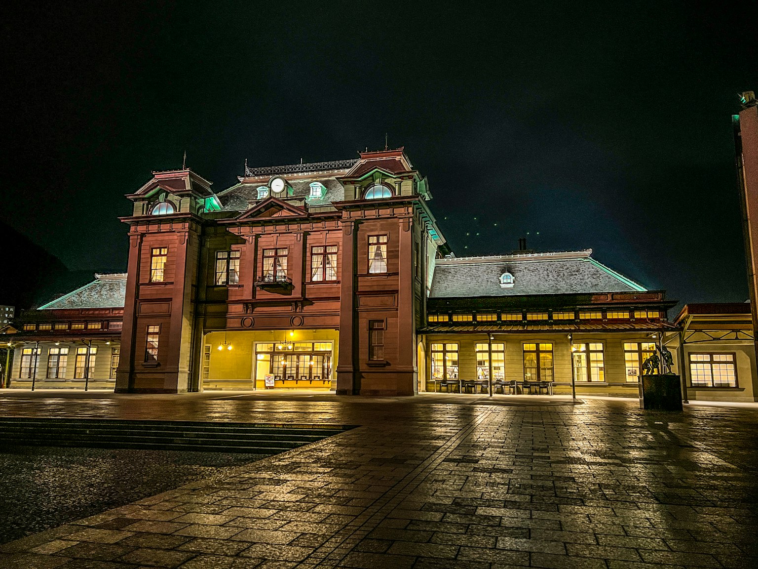 Bâtiment historique en briques rouges illuminé la nuit avec des fenêtres lumineuses et des détails architecturaux
