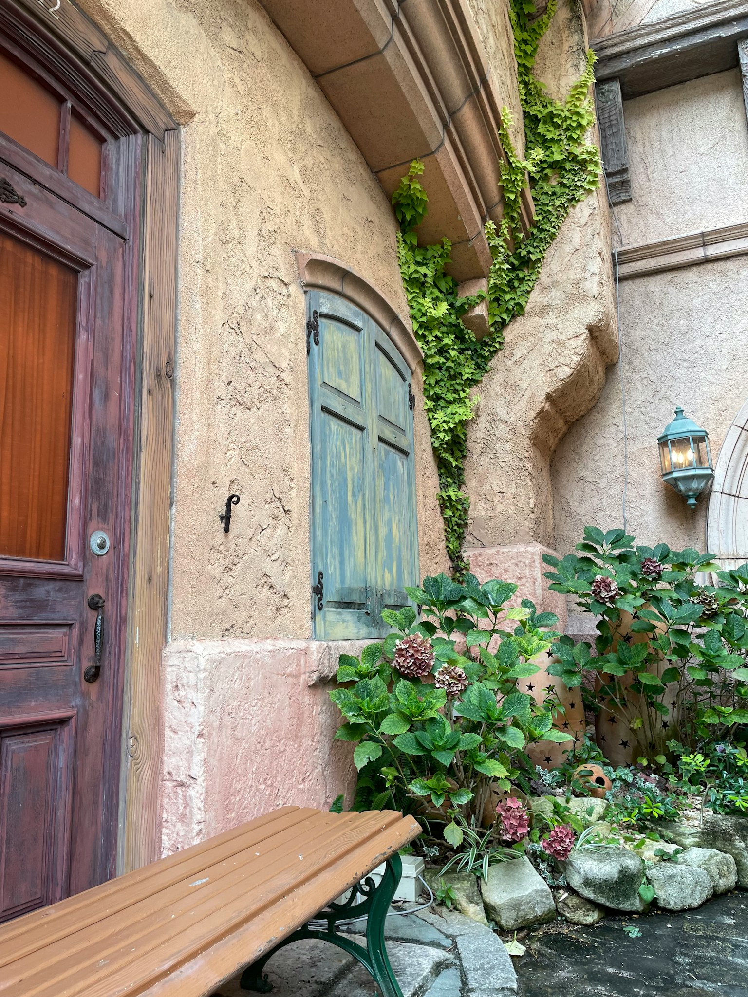 오래된 건물의 입구에 나무 문과 창문이 있으며 녹색 식물과 꽃으로 둘러싸여 있다