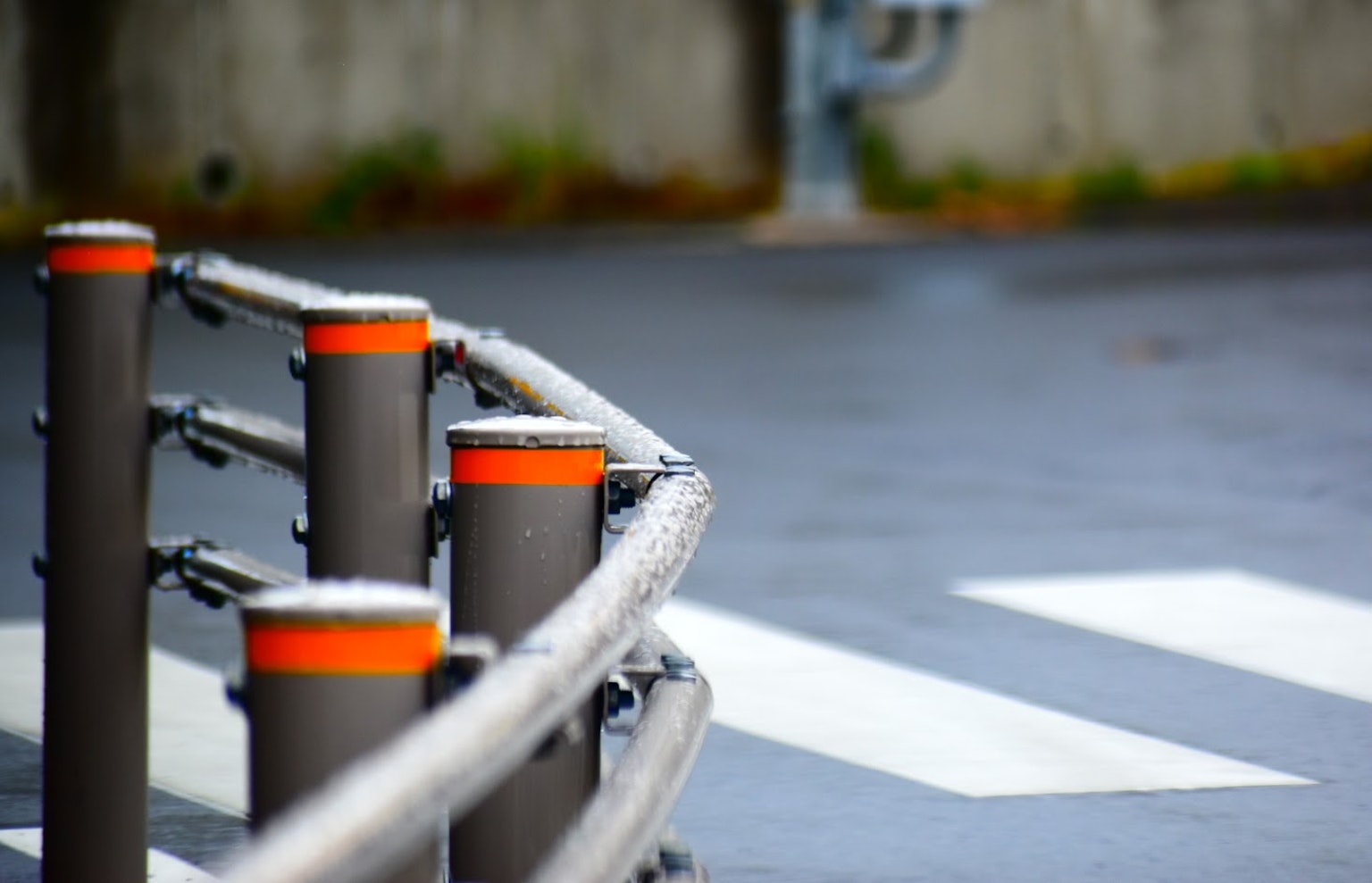 Rambarde grise avec des bouchons orange et passage piéton blanc au premier plan