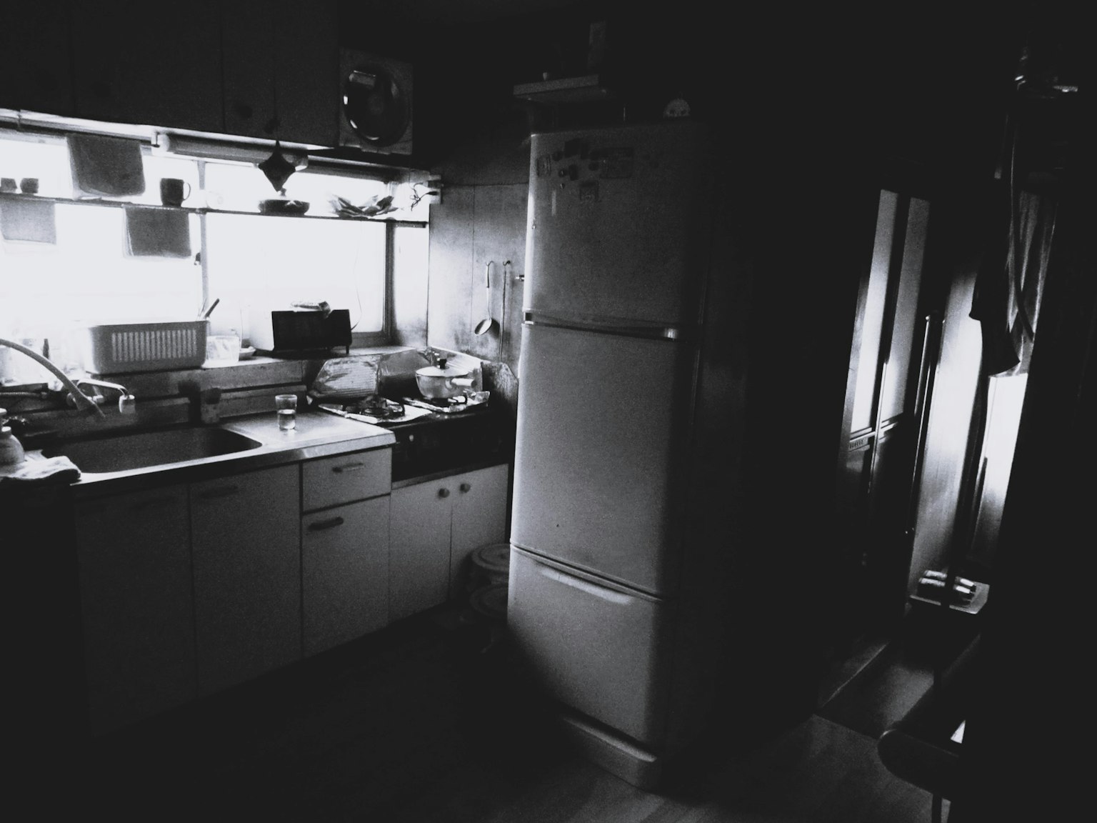 Una cucina poco illuminata con un frigorifero in evidenza e un piano di lavoro semplice
