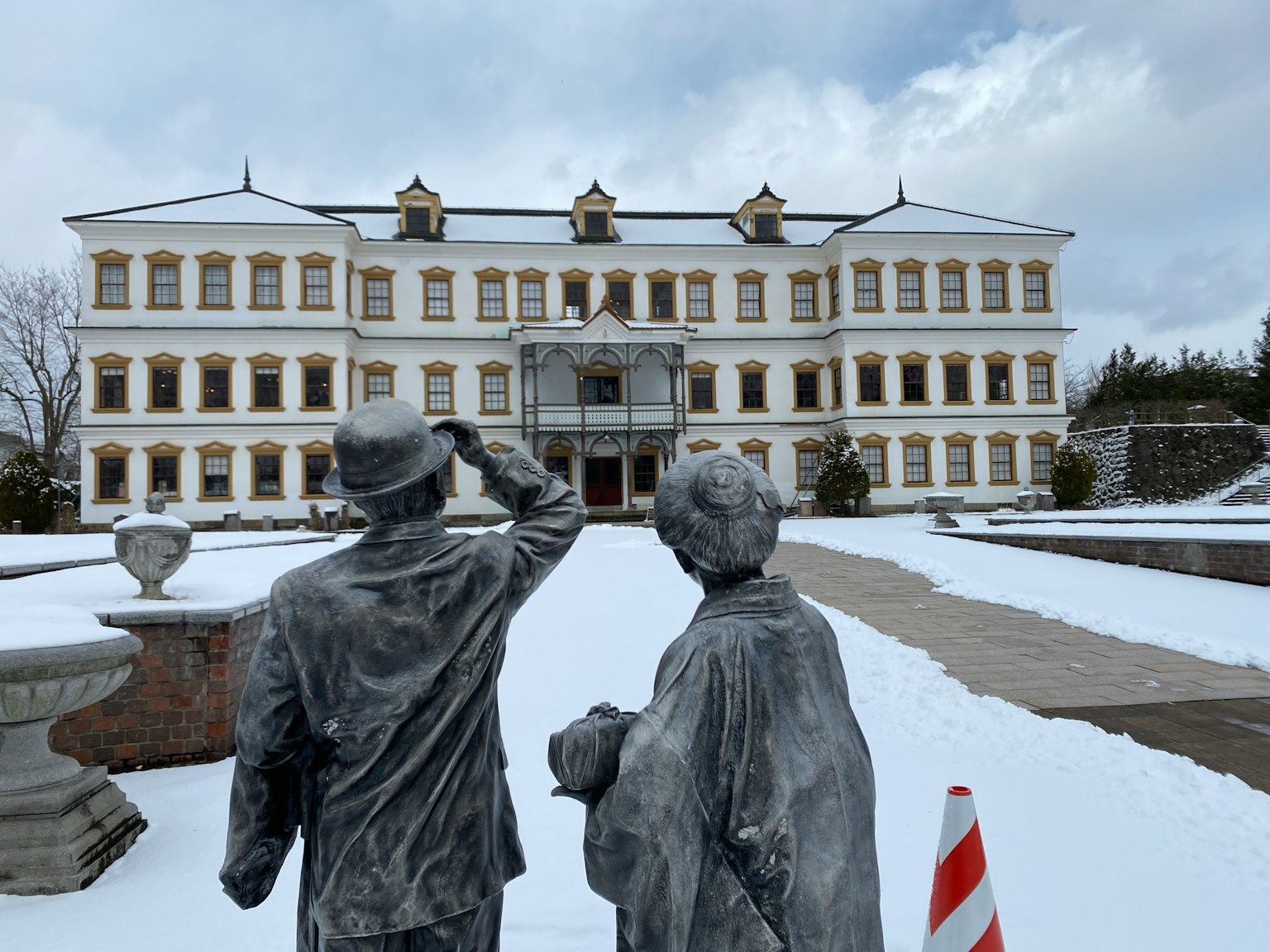 Statue di bronzo di una coppia che osserva un grande edificio in un giardino innevato