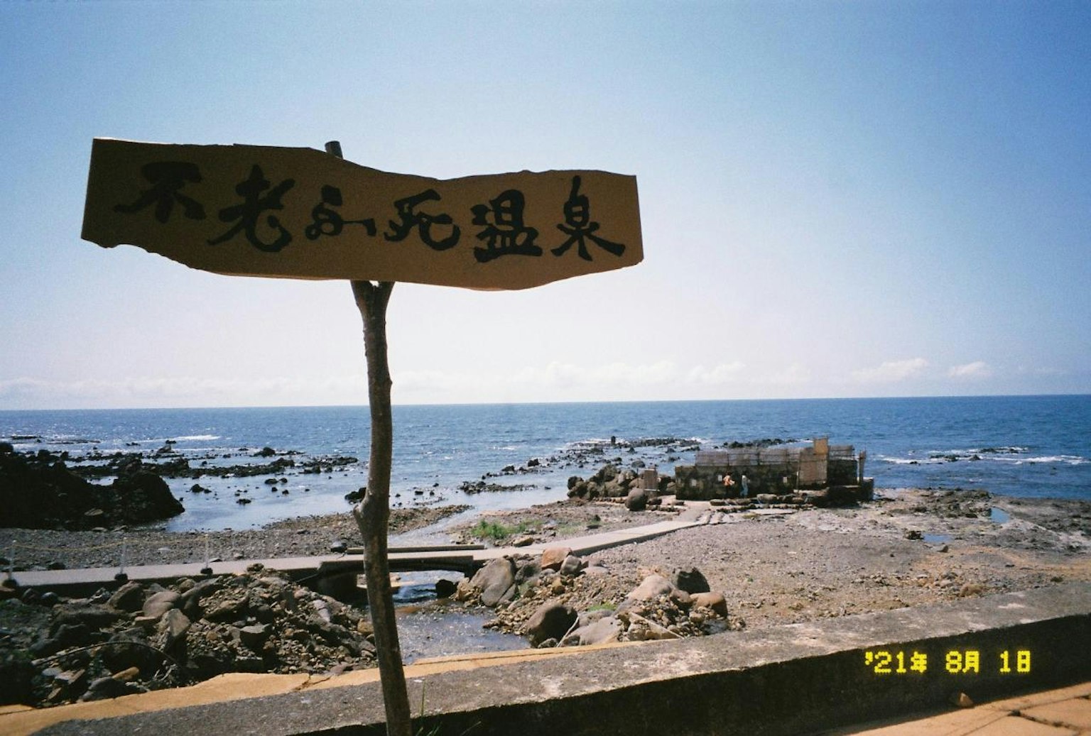 Cartello di legno vicino all'oceano con una spiaggia rocciosa