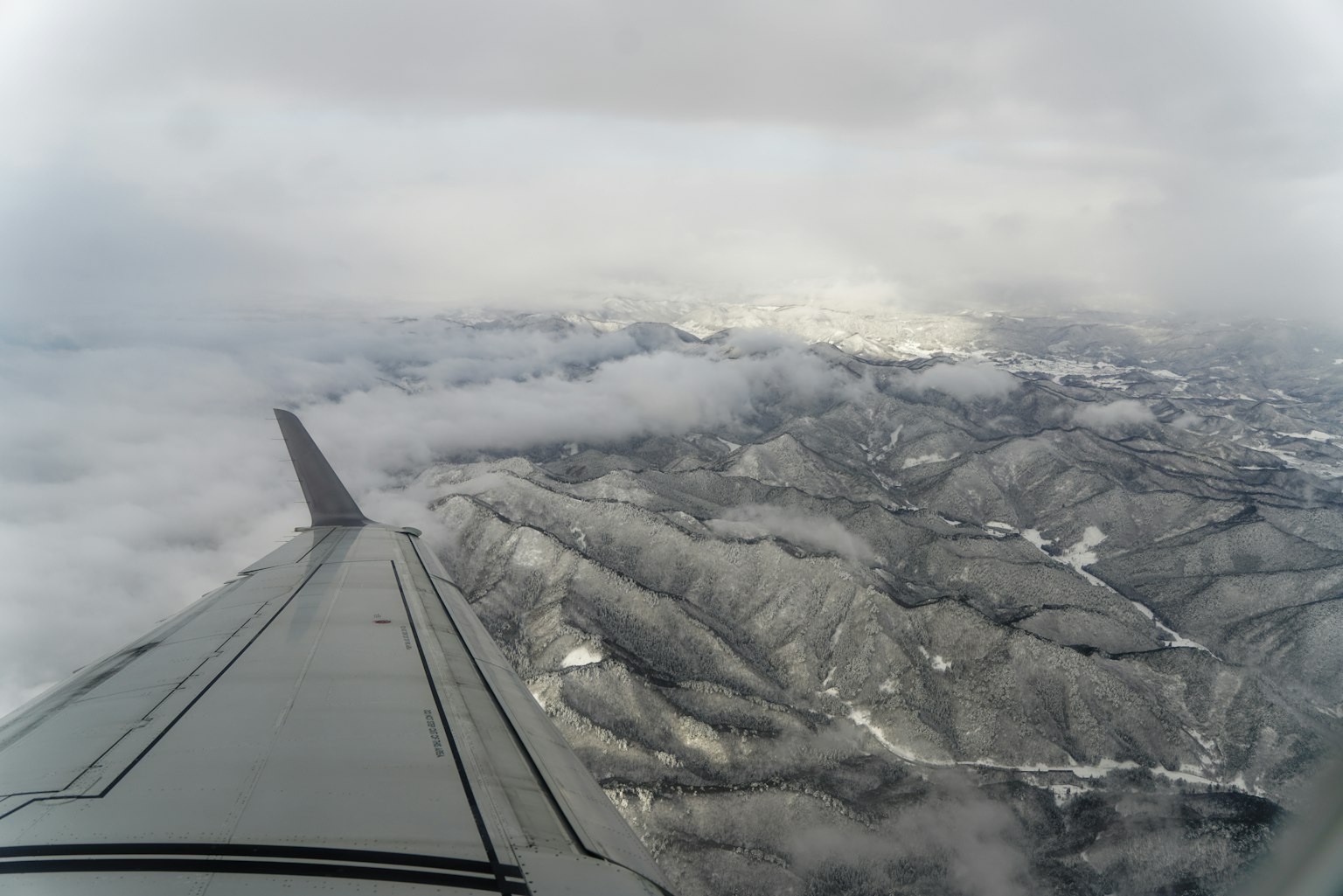 View of snow-covered mountains and clouds from an airplane wing