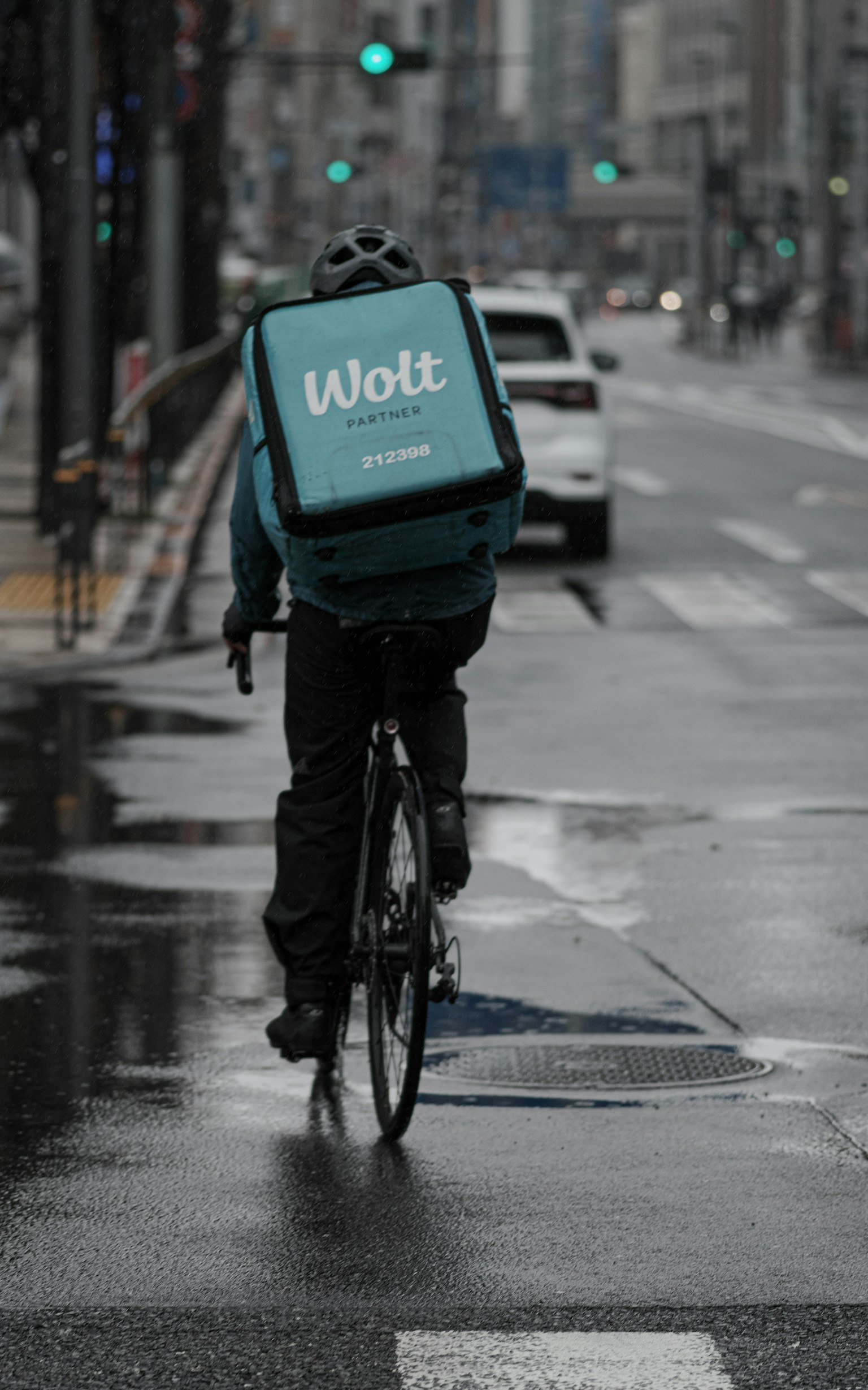 在雨中骑自行车的快递员背着 Wolt 送餐包