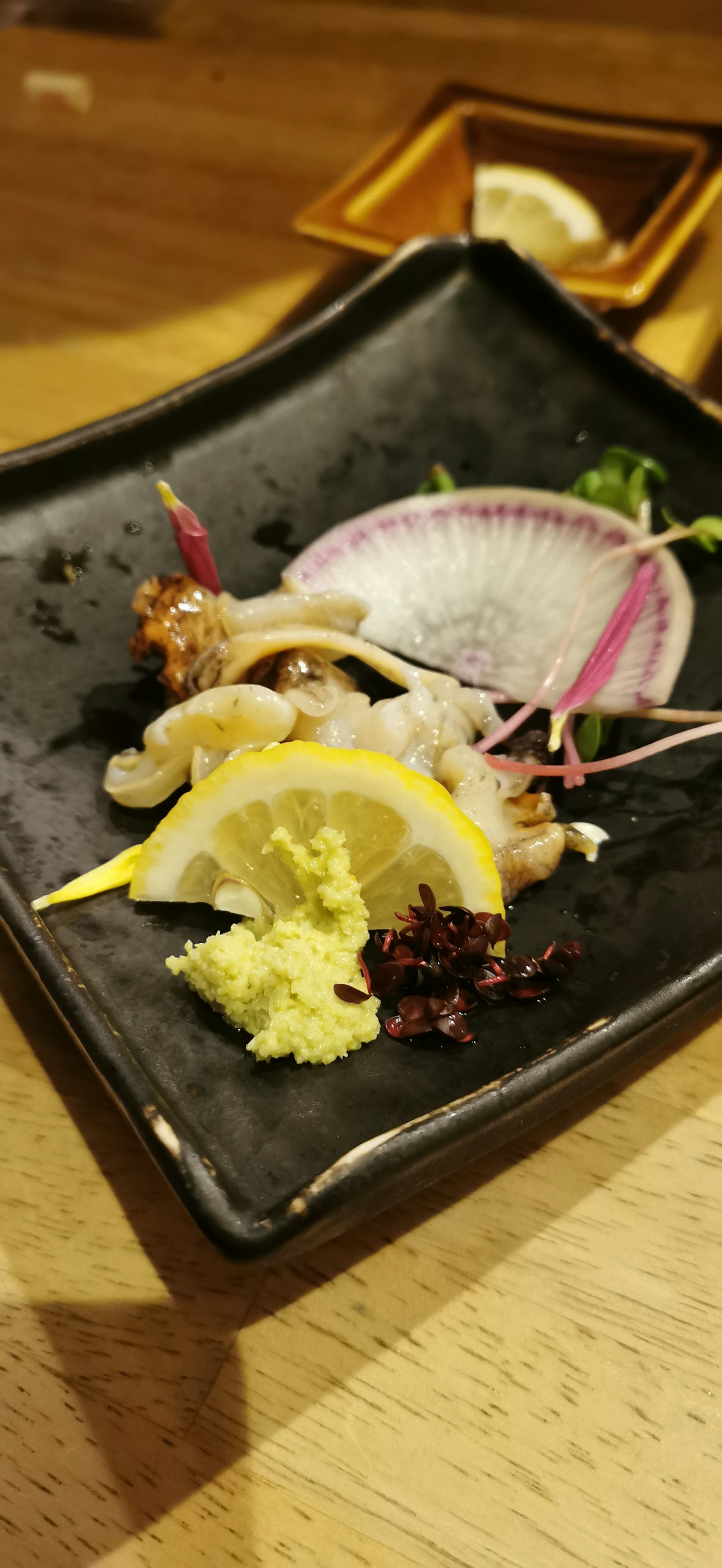 Sashimi frais servi sur une assiette noire avec des tranches de citron