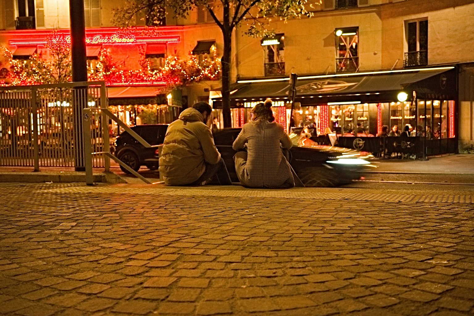 Deux personnes assises dans la rue la nuit avec des lumières de café en arrière-plan