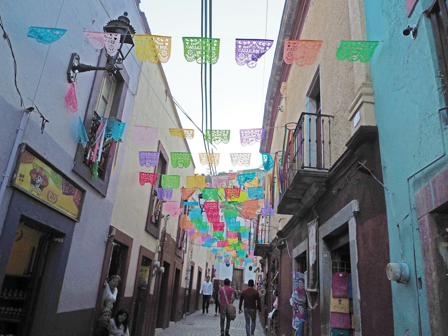 화려한 papel picado 장식이 있는 활기찬 거리에서 사람들이 걷고 있음