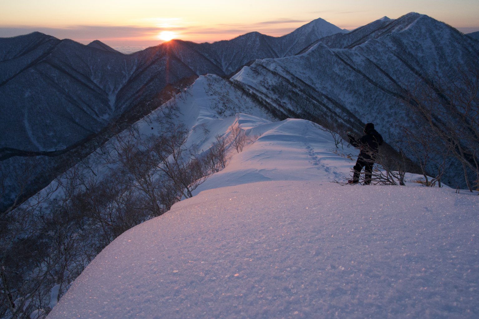 Crête montagneuse enneigée avec un randonneur silhouetté contre le coucher de soleil