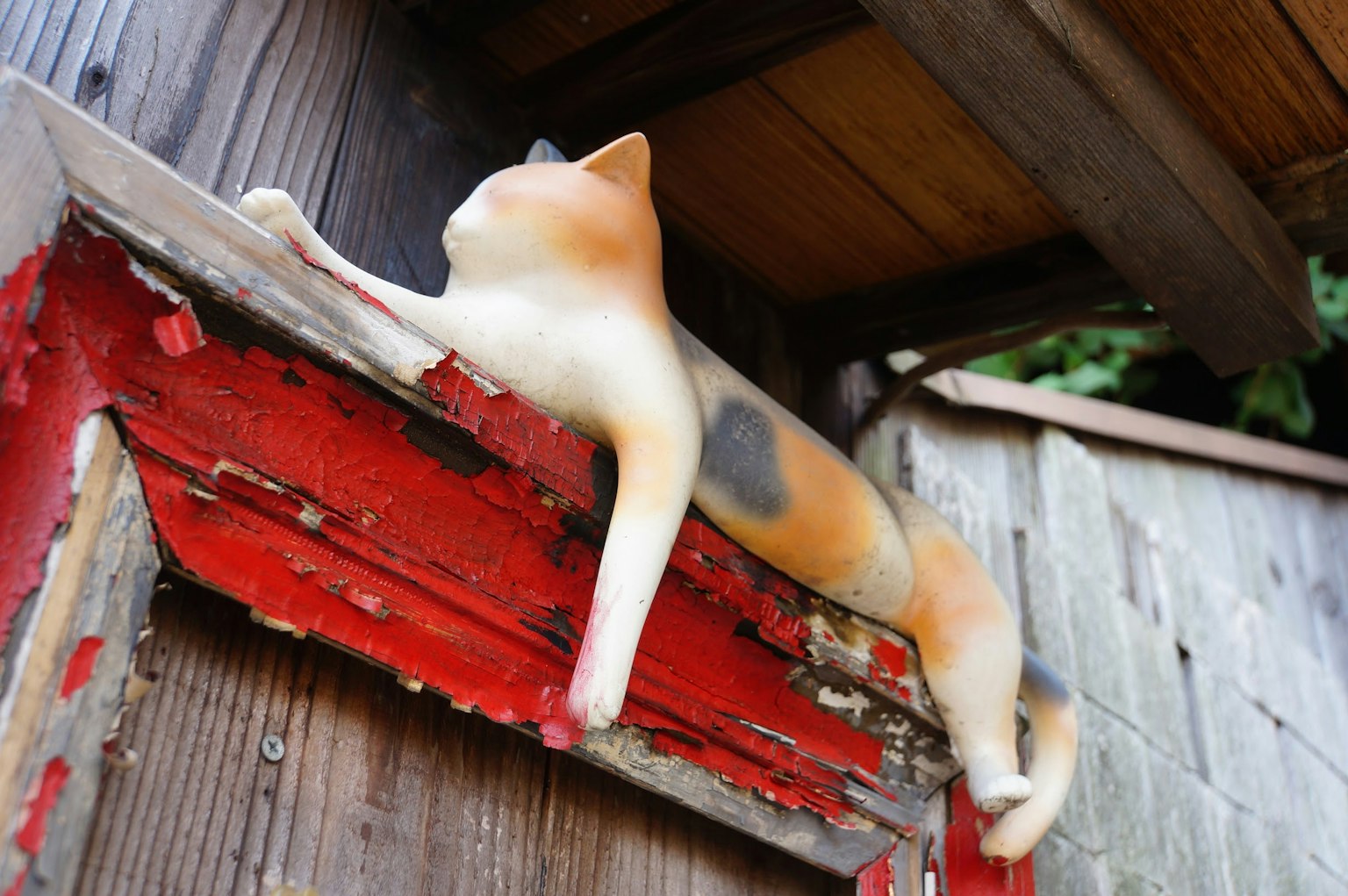 Una scultura di gatto sdraiata su una trave di legno rosso