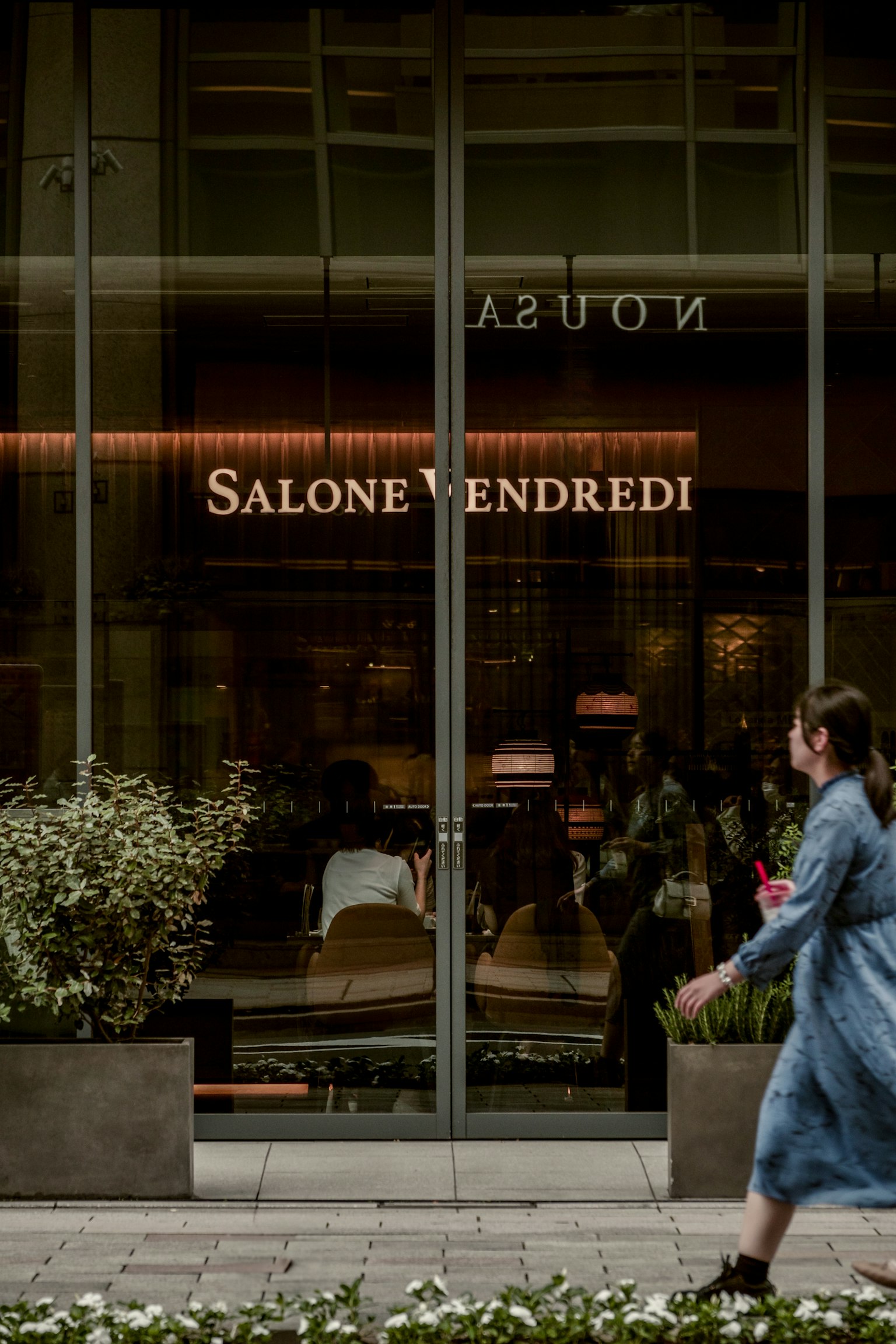 Una donna che cammina davanti alla vetrina di Salone Vendredi con piante in primo piano