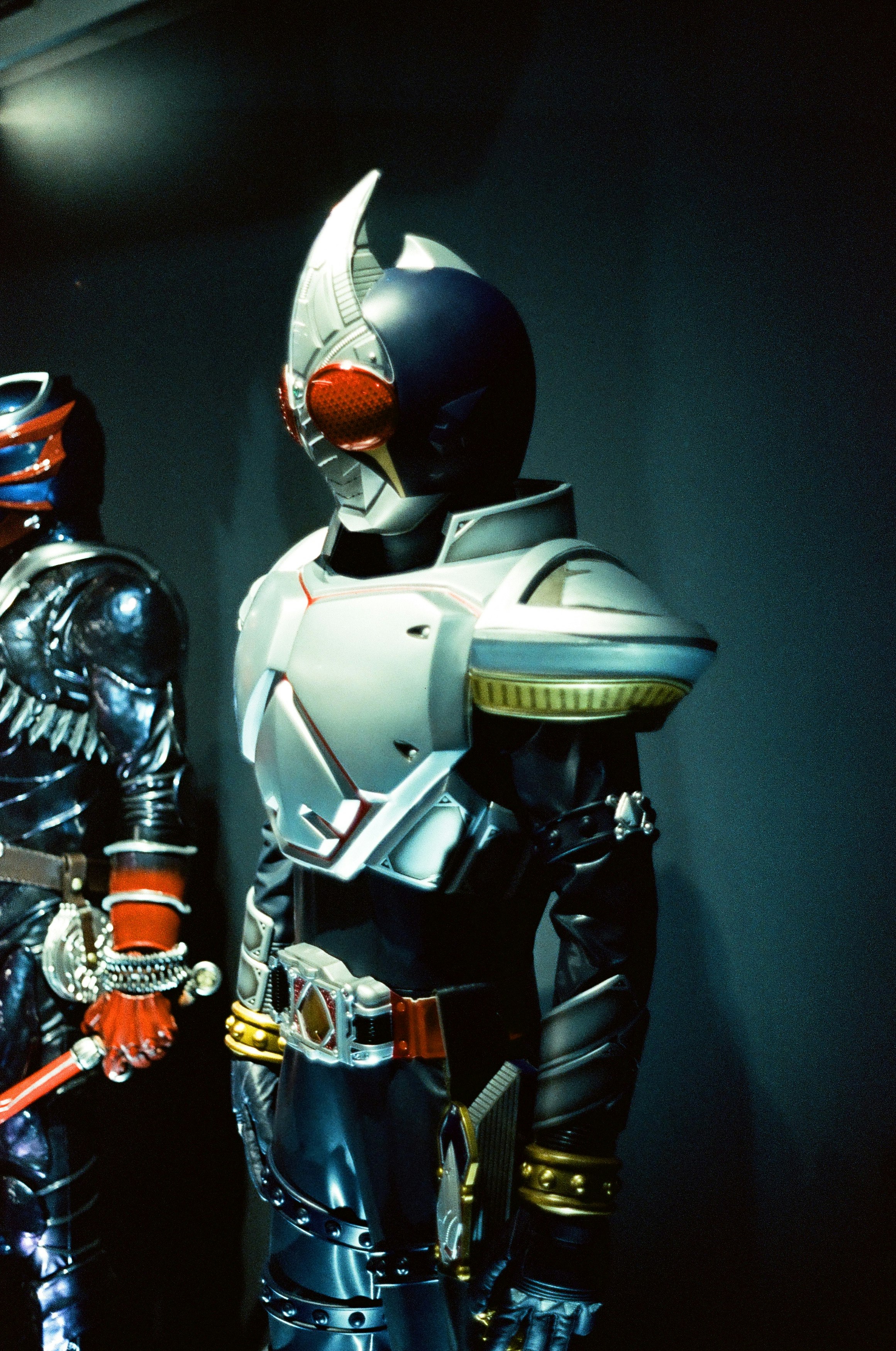 展示室で並ぶ仮面ライダー風のスーツとフィギュア