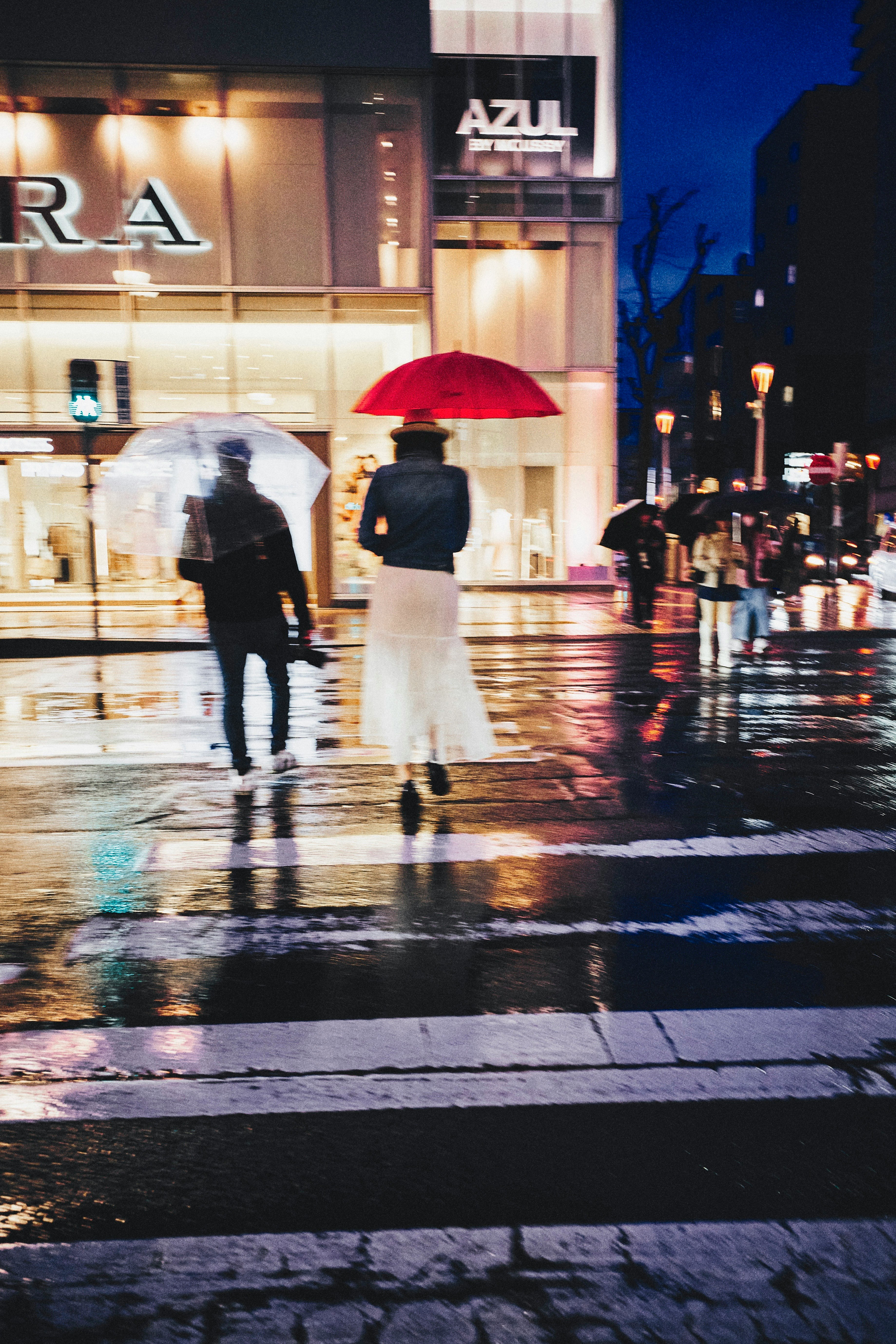 雨上がりの街角で傘をさす人とショーウィンドウの並ぶ通り