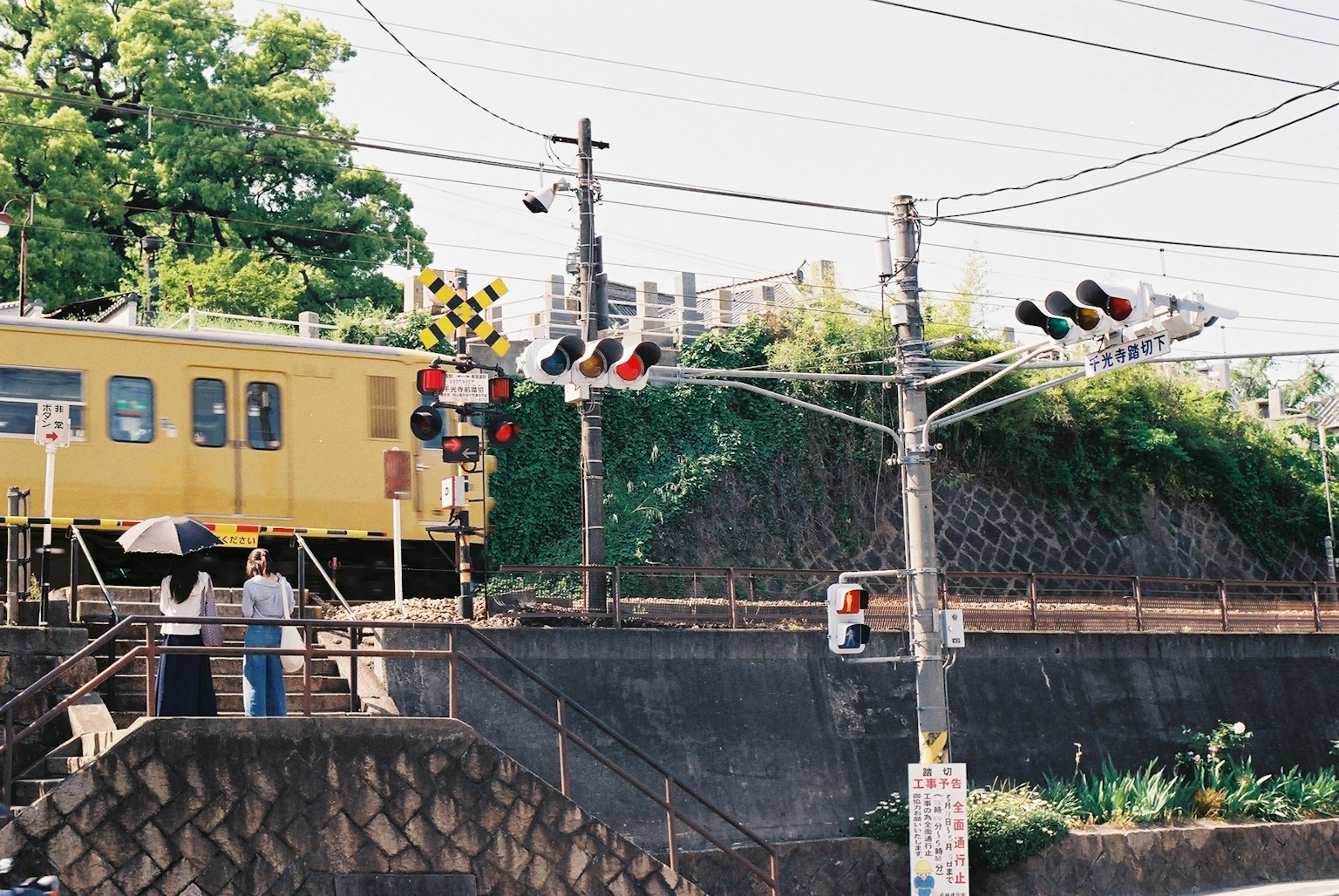 Scene of a yellow train passing a level crossing with people waiting