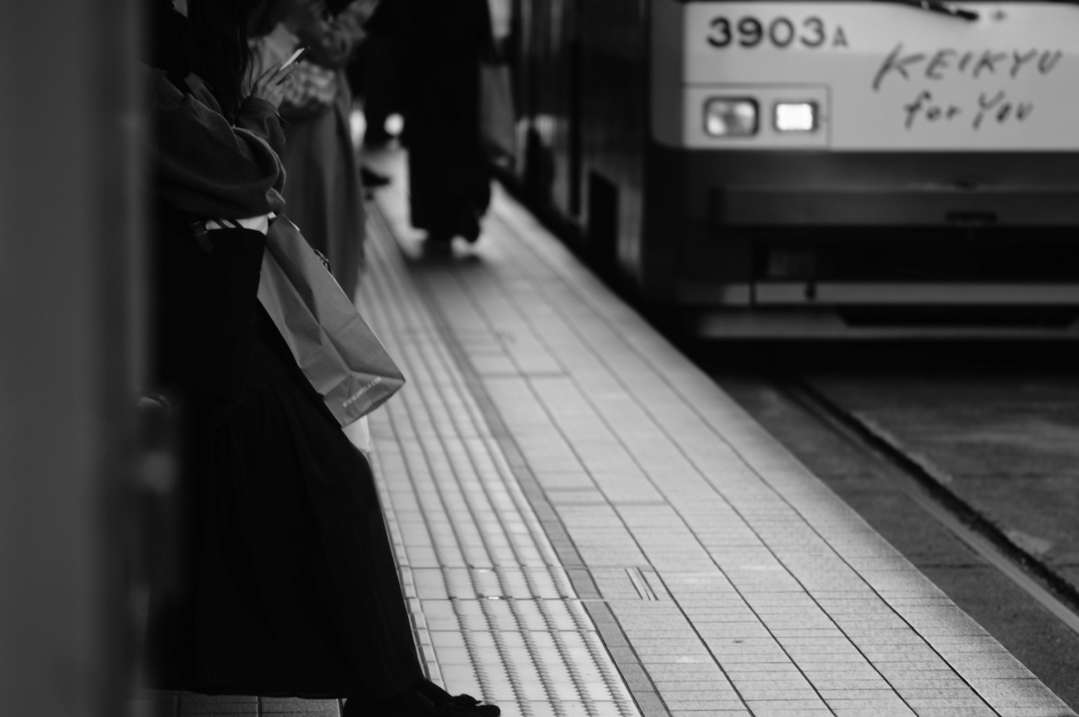 Black and white image of people waiting at a train station with visible feet and platform