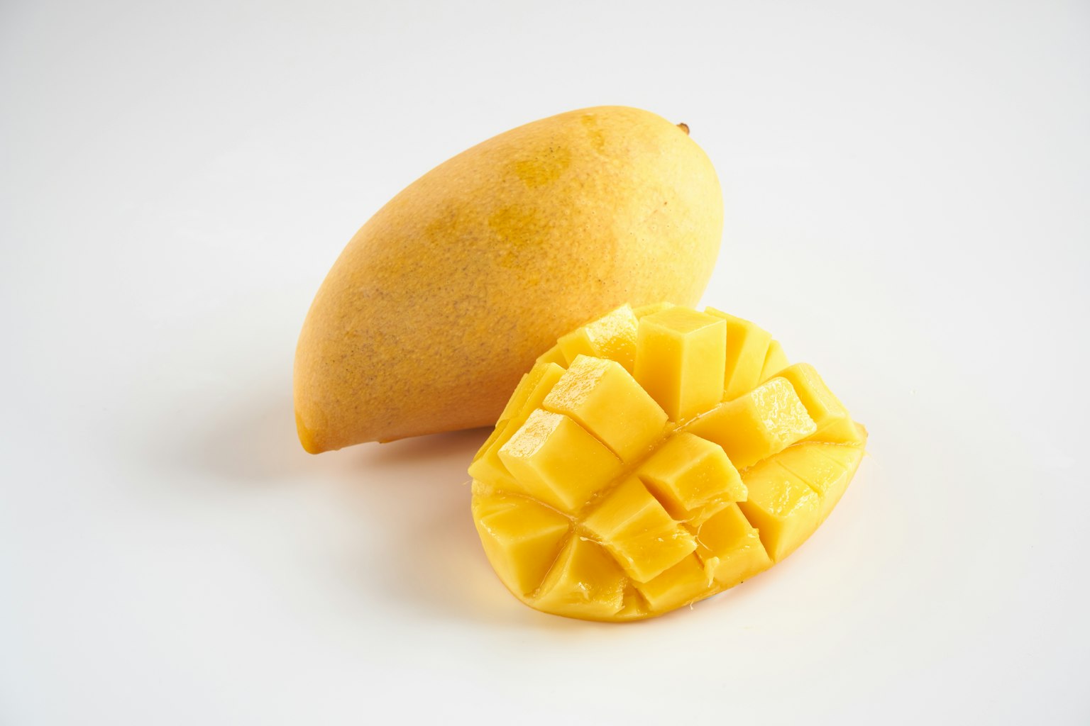 Una mango intera e una metà di mango affettata su uno sfondo bianco