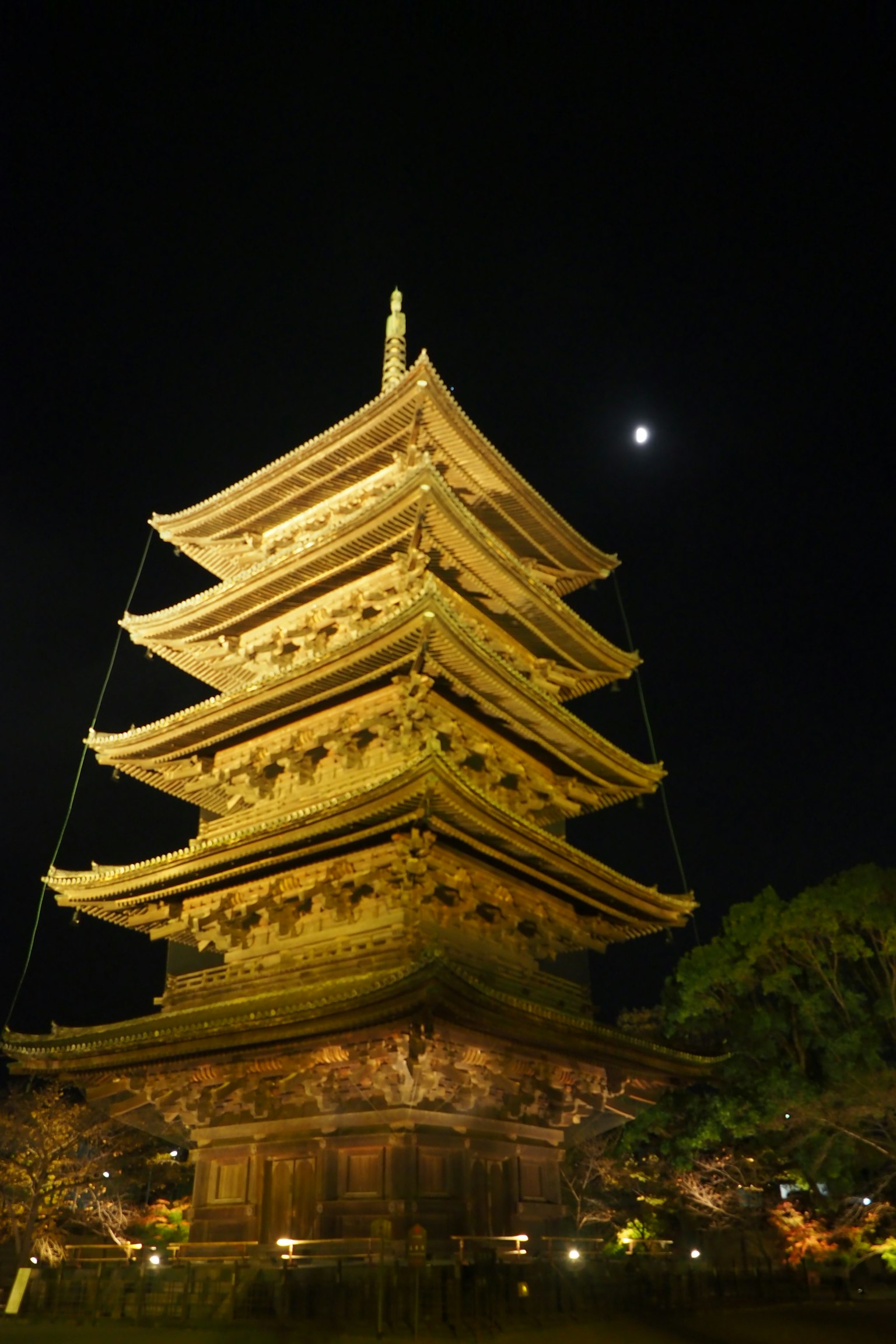 Illuminated five-story pagoda under a night sky with a crescent moon