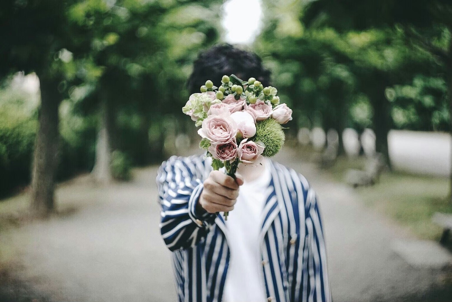 Persona con giacca a righe che tiene un mazzo di fiori in un parco