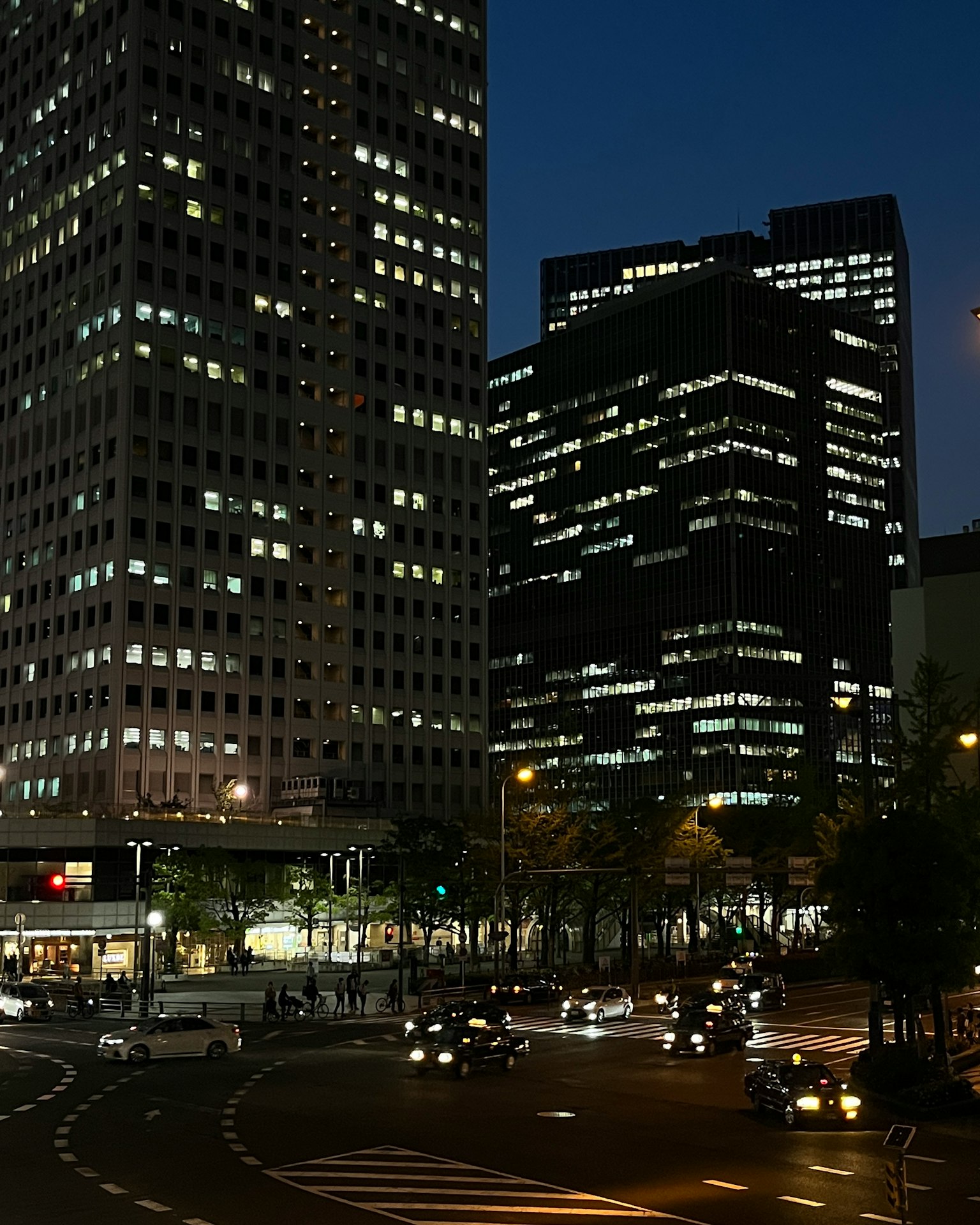 Nächtliche Stadtlandschaft mit hohen Wolkenkratzern, beleuchtet von Autolichtern an einer Kreuzung