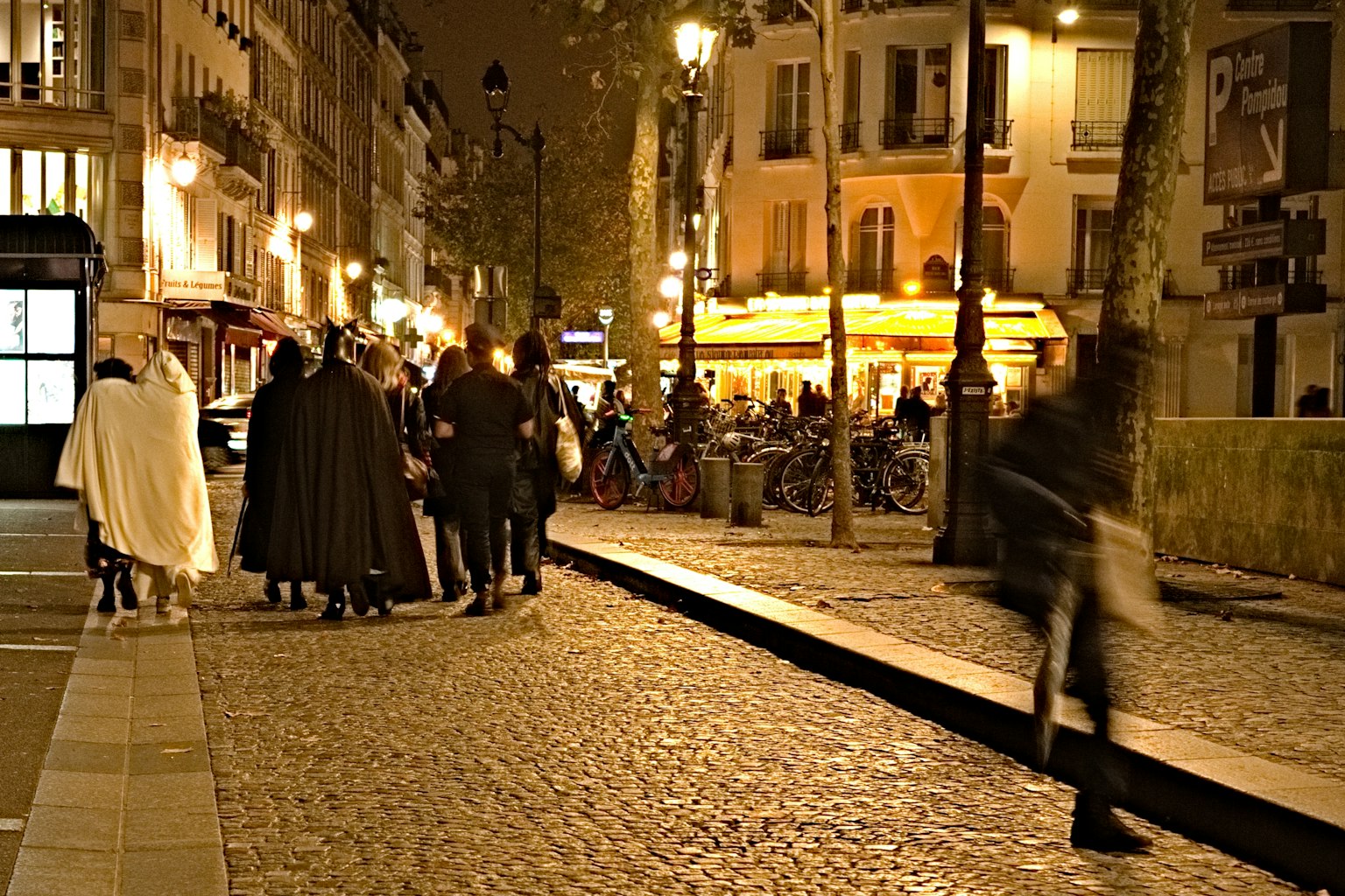 Persone che camminano su una strada lastricata a Parigi di notte con un caffè illuminato
