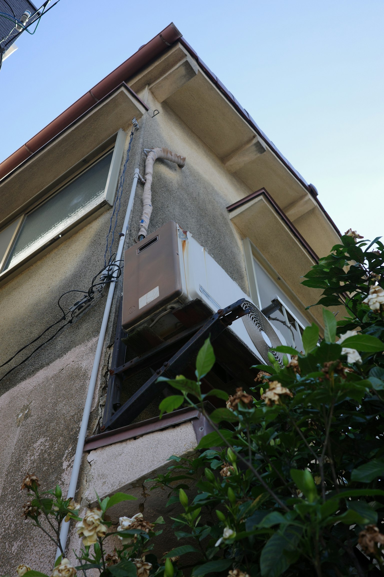 Side view of an old building with an air conditioning unit and green foliage