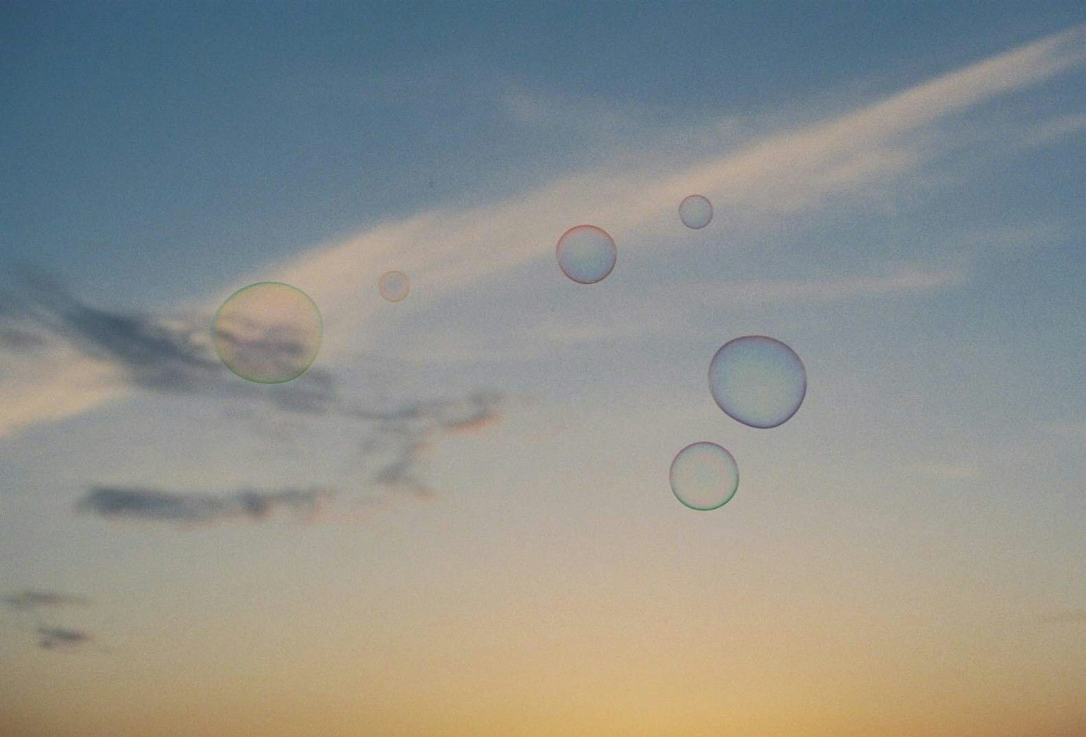 Burbujas flotando en un cielo azul con nubes suaves al atardecer