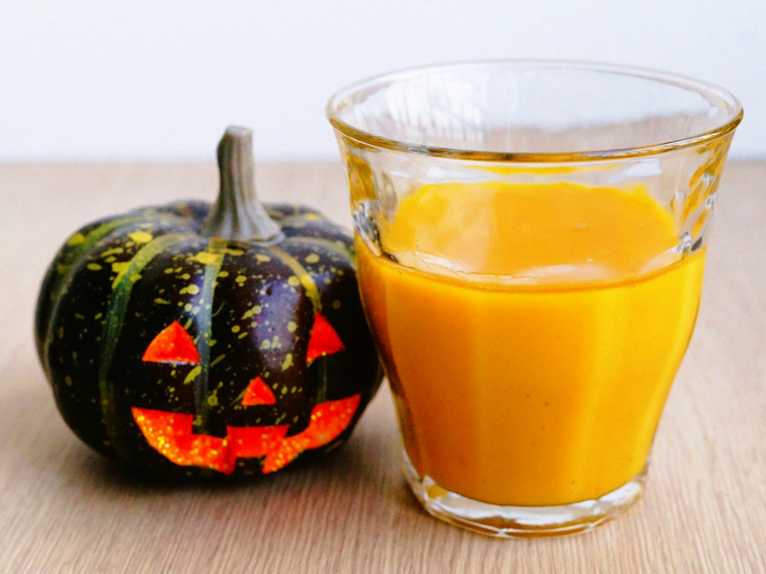 Calabaza decorada para Halloween con una cara tallada y un vaso de jugo de naranja