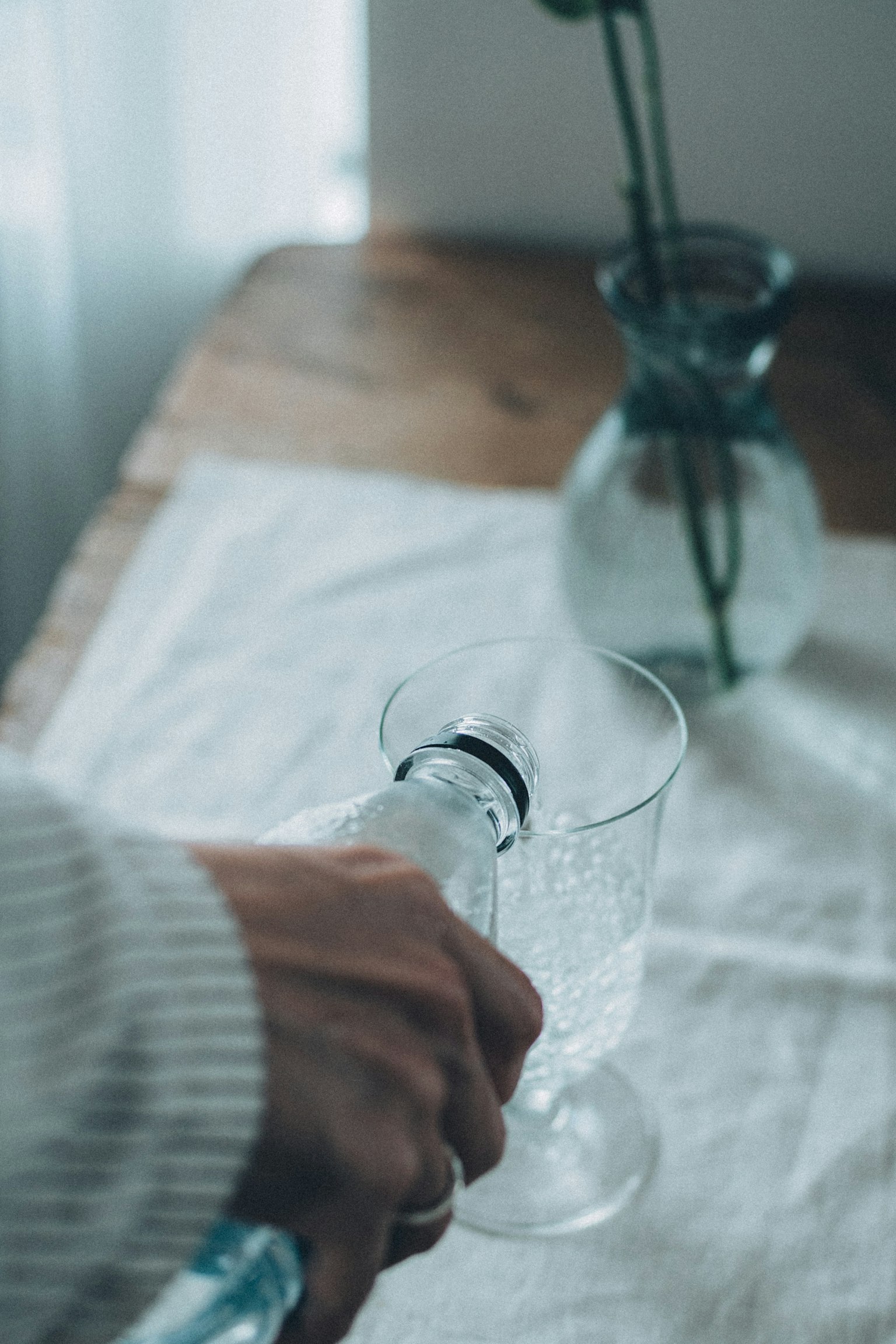 手将水倒入透明玻璃杯,背景有花瓶