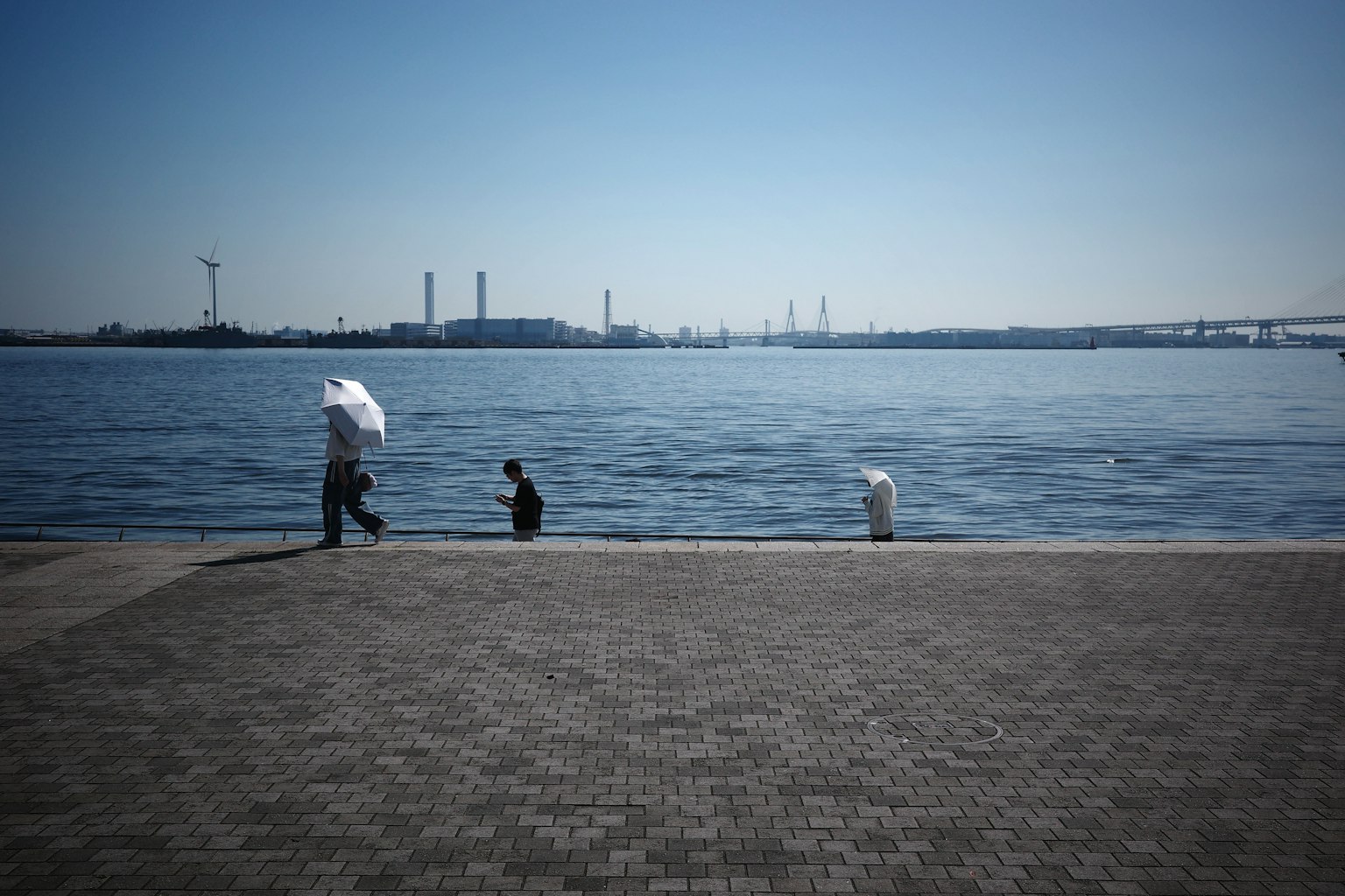 People by the water with a factory skyline